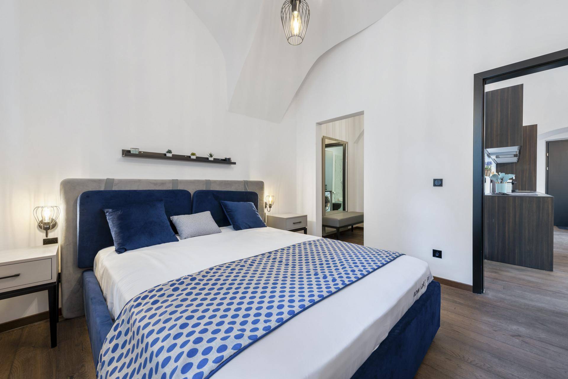 Helles Schlafzimmer mit blauem Bett, Holzboden und einer eleganten Gewölbedecke.