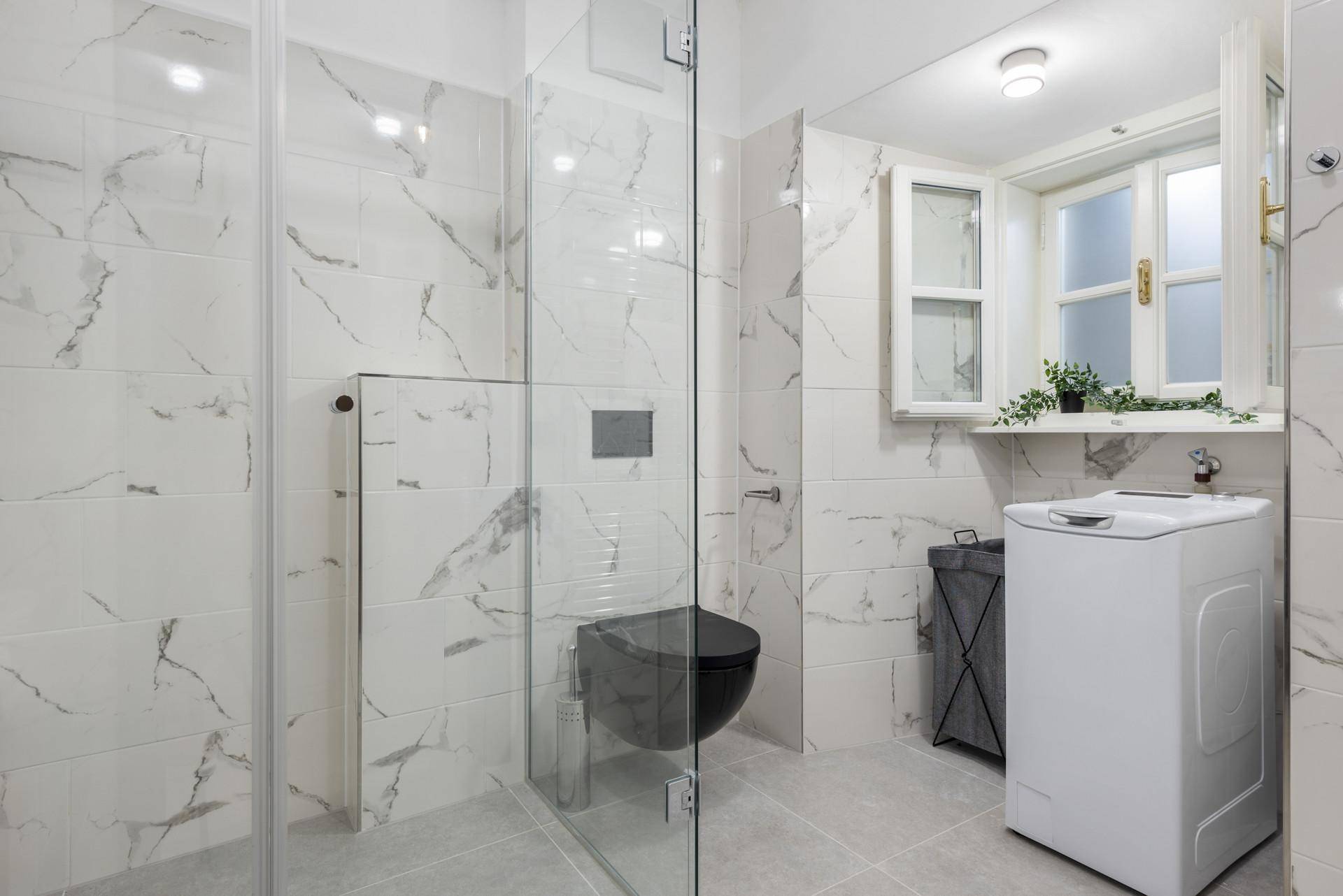Modernes Badezimmer mit begehbarer Dusche, Marmorfliesen und integrierter Waschmaschine.