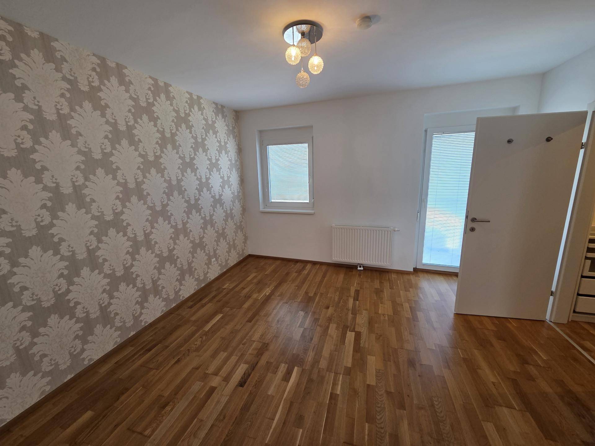 Geräumiges Schlafzimmer mit Holzboden und einer Akzentwand mit floraler Tapete.
