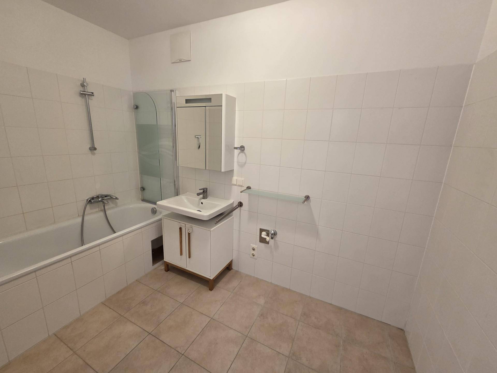 Badezimmer mit Badewanne, Waschbecken und weißen Fliesen an Wänden und Boden.
