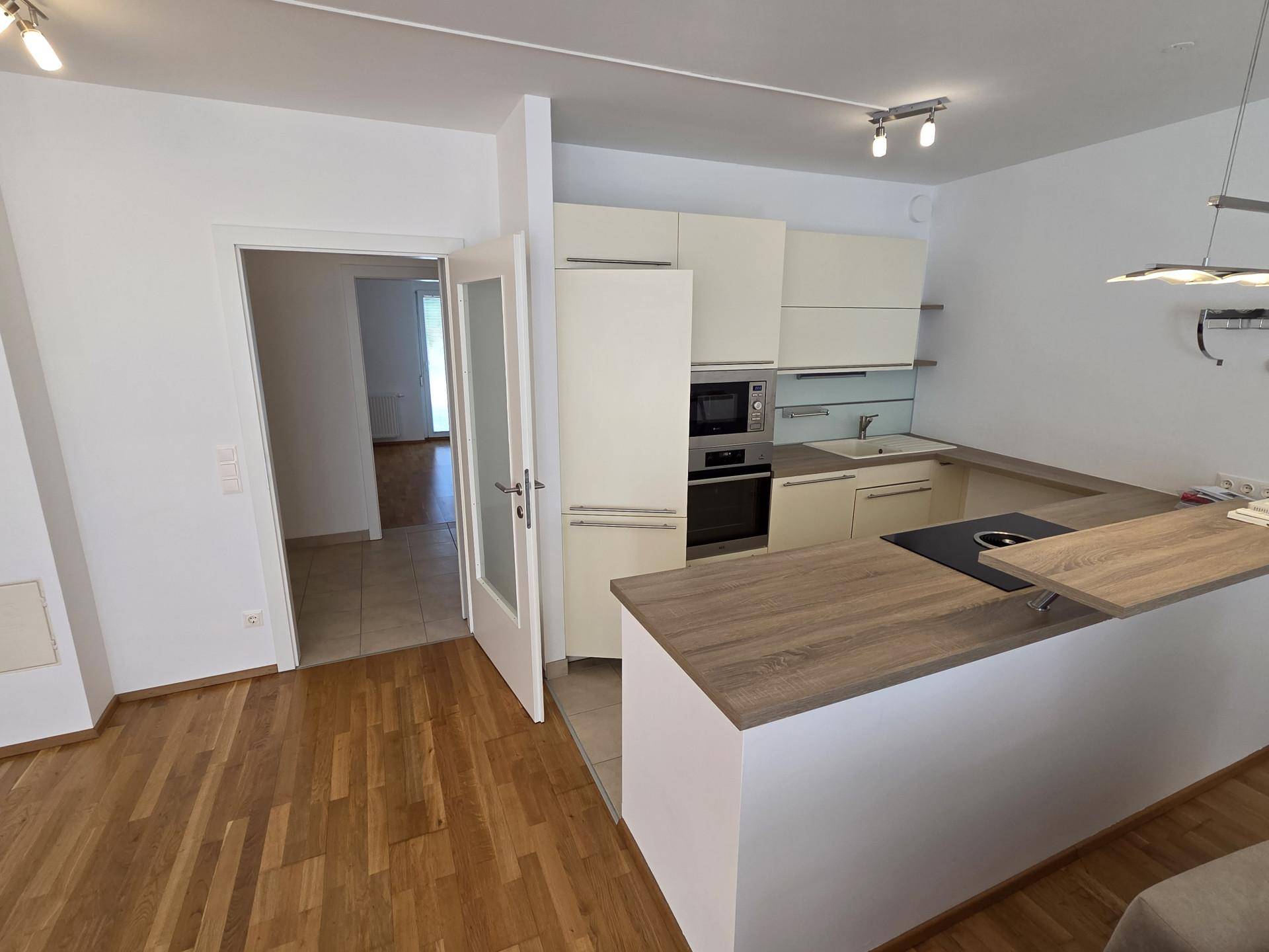 Offener Wohnbereich mit integrierter Küche und Zugang zu einem weiteren Zimmer mit Fliesenboden.