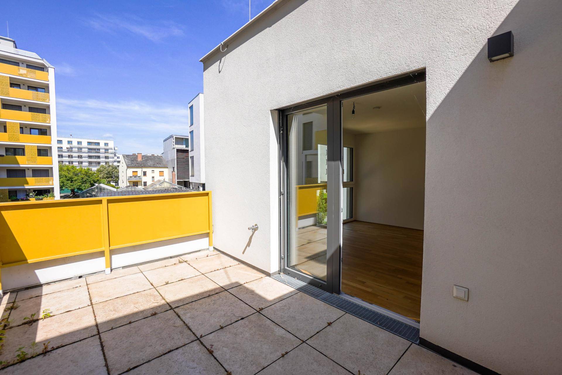 Balkon mit Fliesenboden und Schiebetür, bietet Zugang zu einem hellen Innenraum.