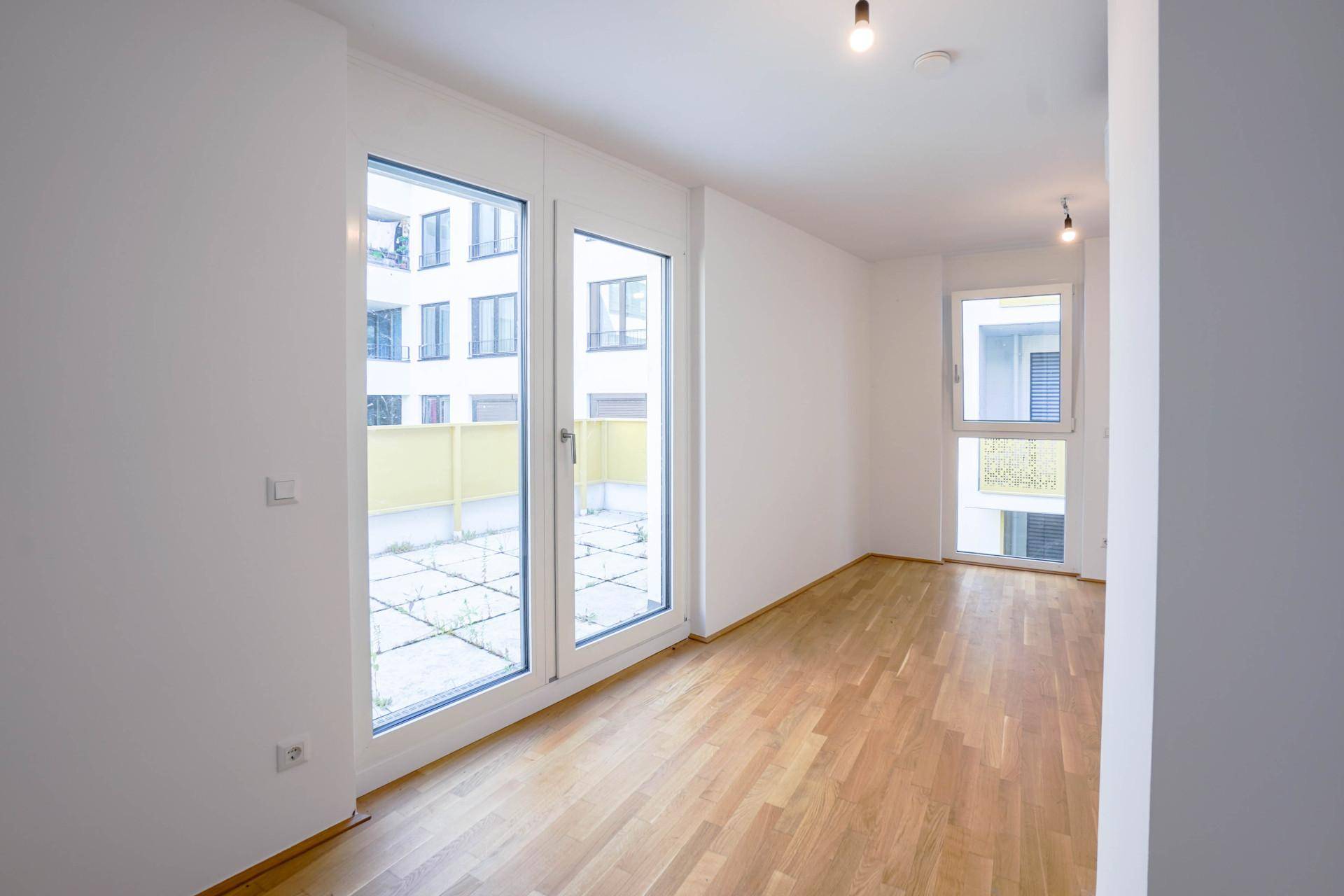 Heller Wohnraum mit großen Fenstern, Holzboden und Zugang zu einem Außenbereich.