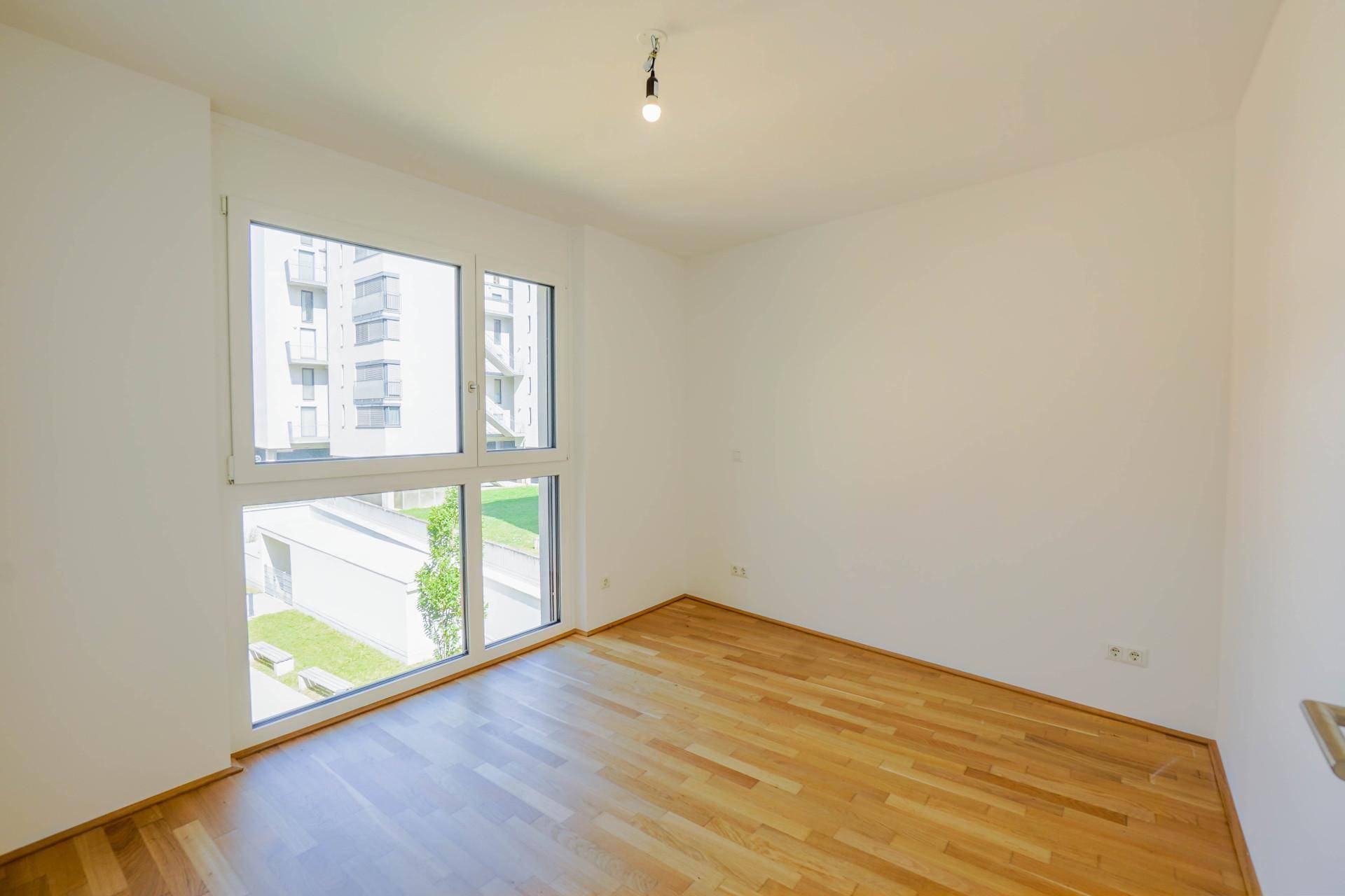 Helles Schlafzimmer mit großen Fenstern und Holzboden, bietet einen Blick ins Grüne.