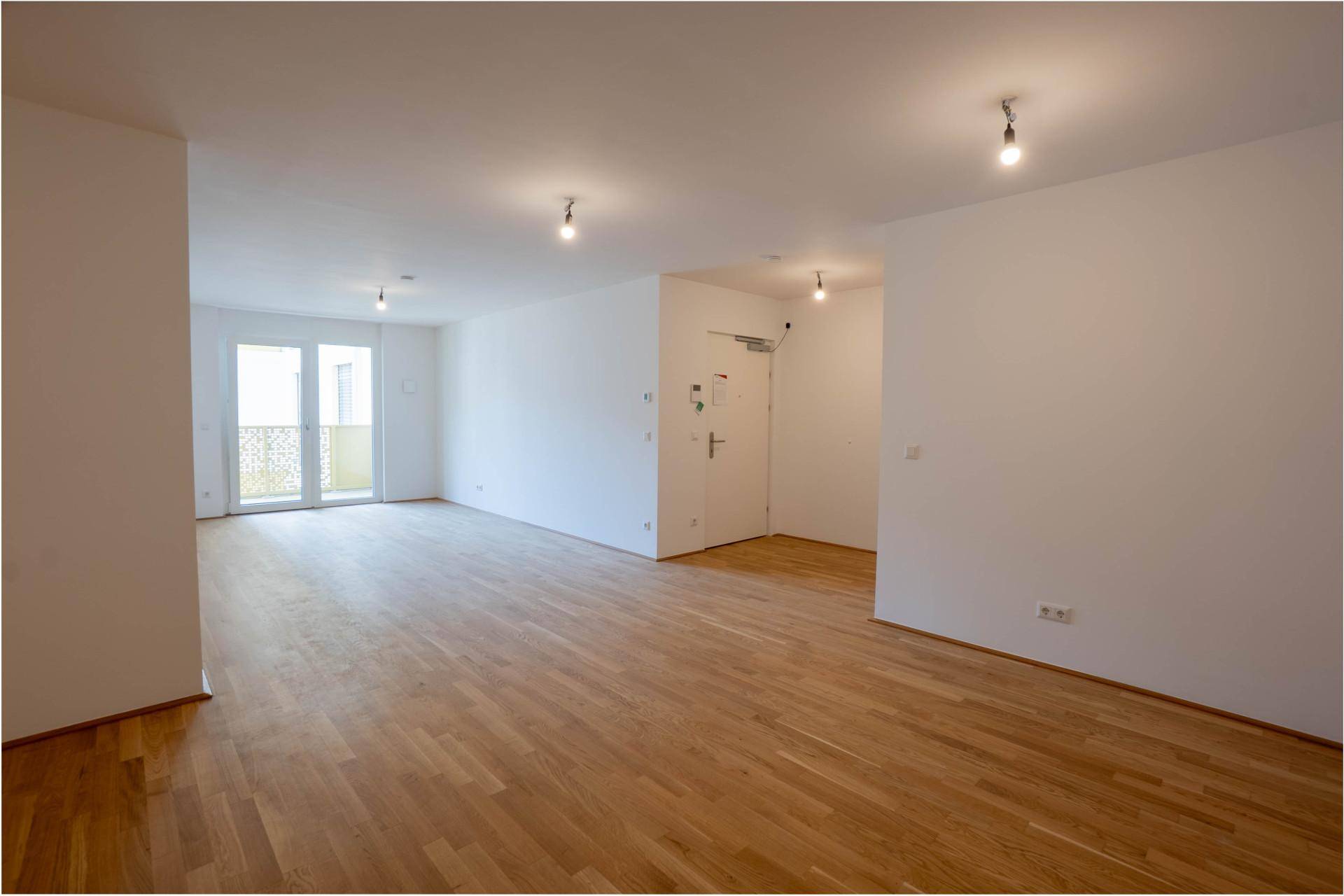 Geräumiger, leerer Wohnbereich mit hellem Parkettboden und viel Tageslicht durch die Balkontür.