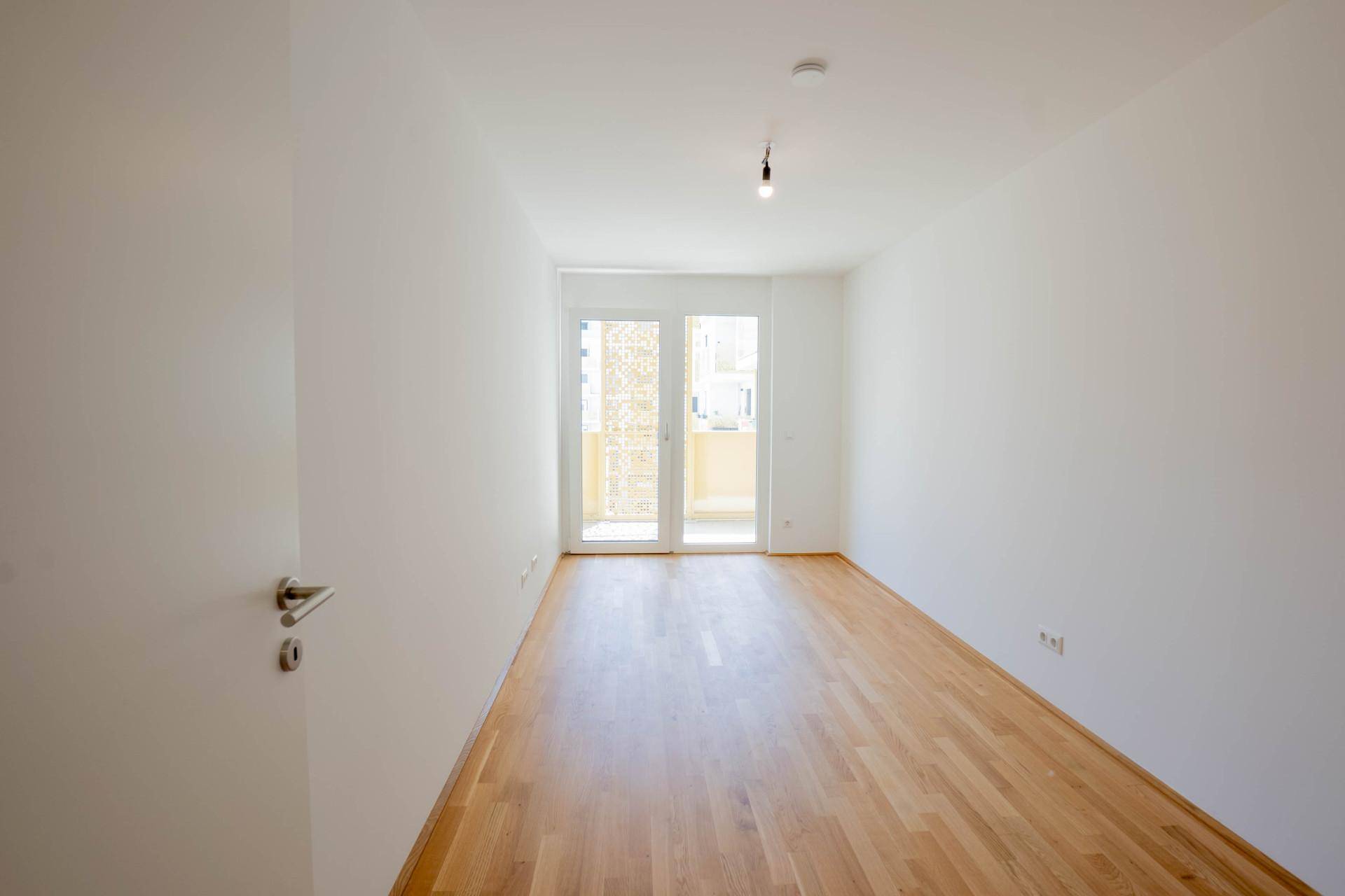 Leeres Zimmer mit hellem Parkettboden und Zugang zu einem Balkon, ideal für individuelle Gestaltung.