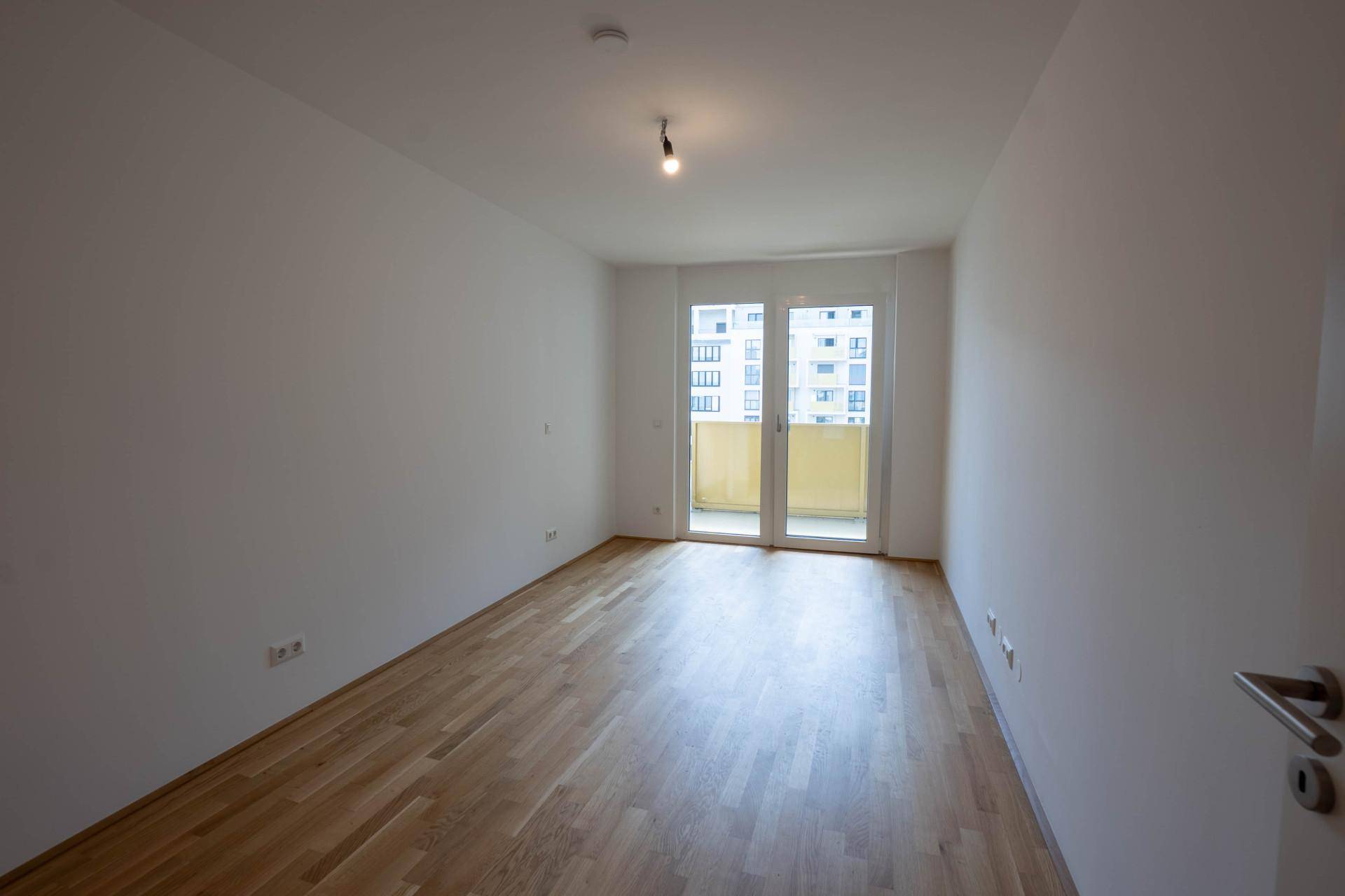 Helles, leeres Zimmer mit Parkettboden und Balkonzugang, bereit für die persönliche Einrichtung.