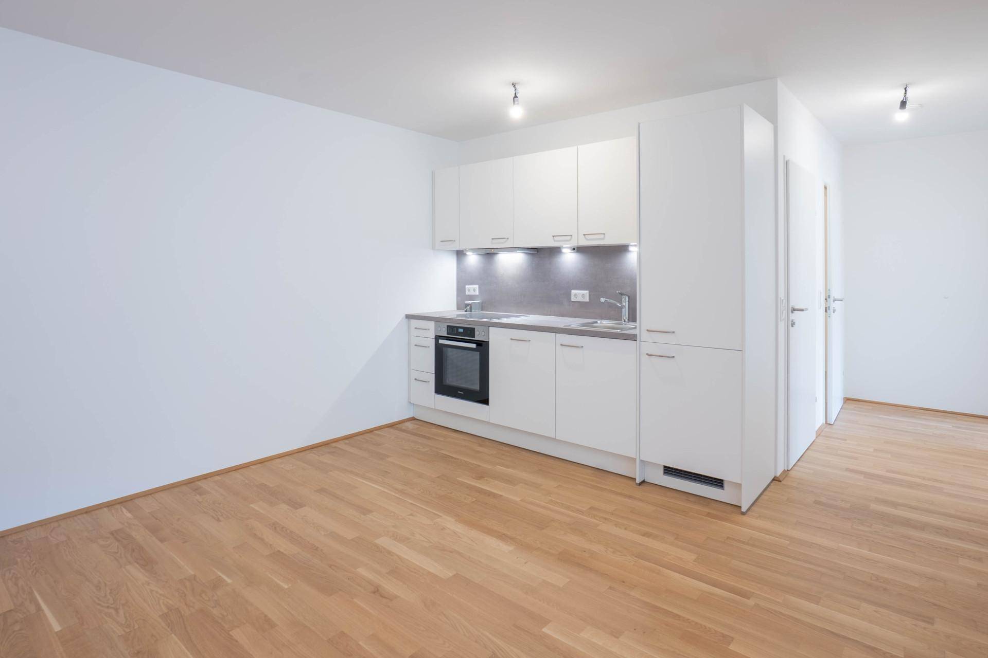 Helle, moderne Küchenzeile mit weißen Schränken und Holzboden in einem offenen Wohnbereich.