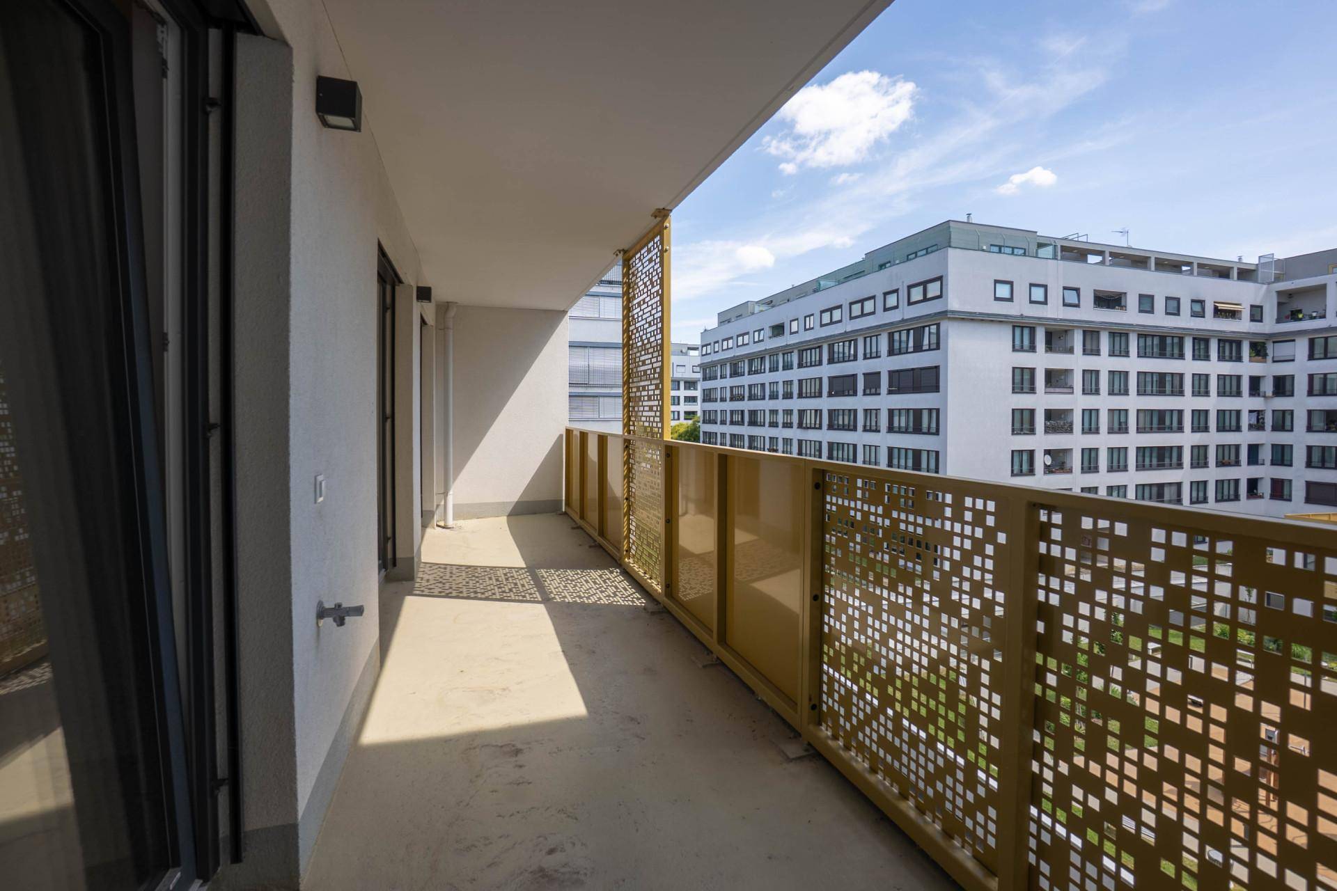 Heller Balkon mit modernem, perforiertem Geländer und Blick auf umliegende Stadtgebäude.