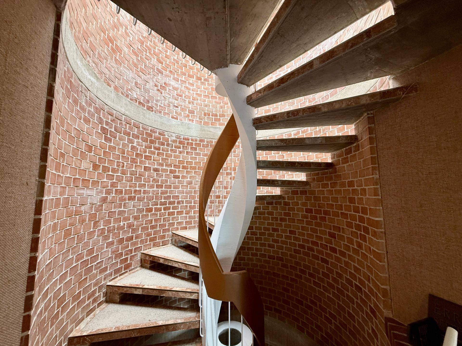Beeindruckende Wendeltreppe aus Beton mit Ziegelwand und Holzgeländer, verbindet die verschiedenen Stockwerke des Hauses.