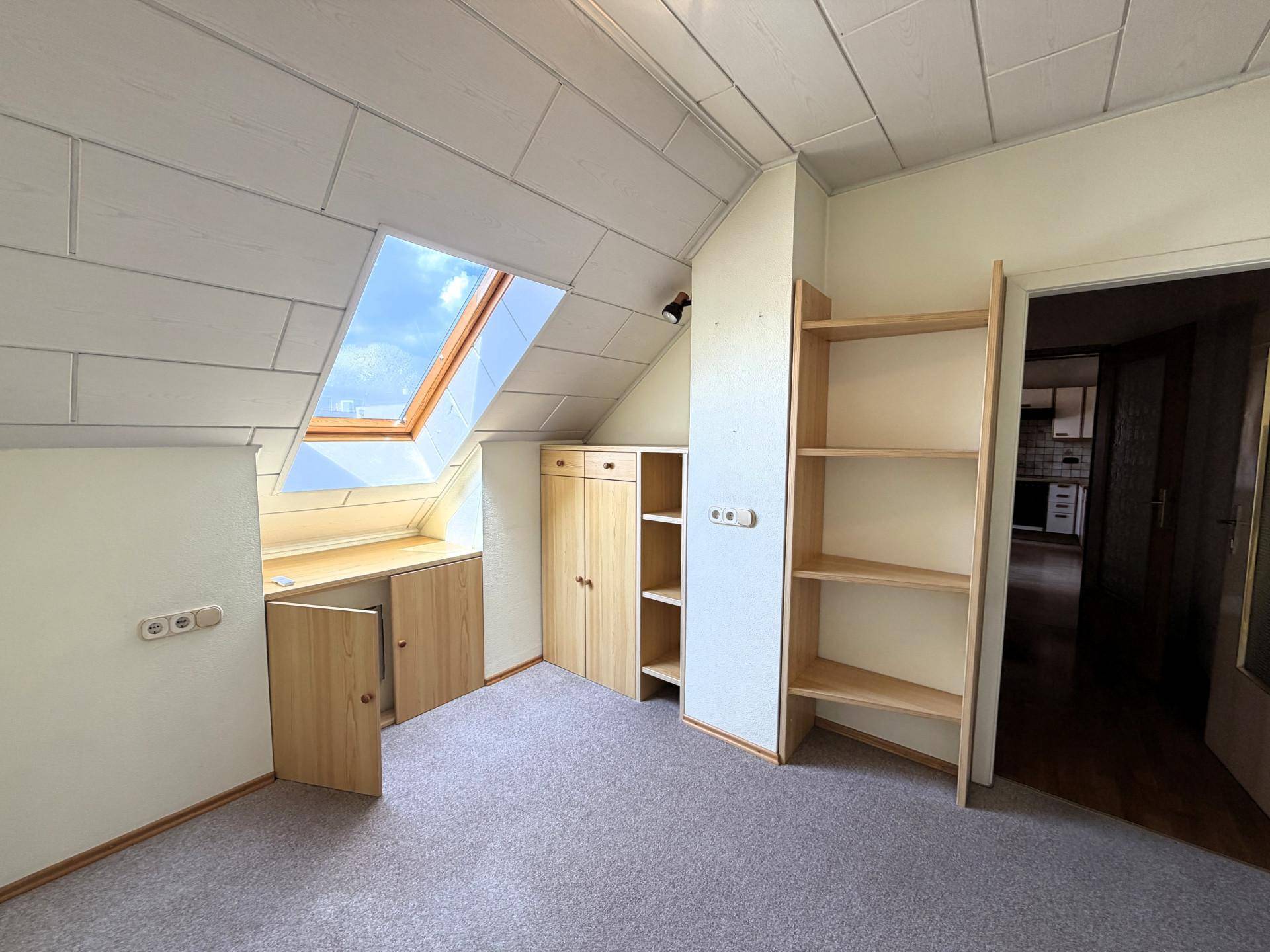 Dachzimmer mit Dachfenster, Teppichboden und praktischen Einbauschränken.