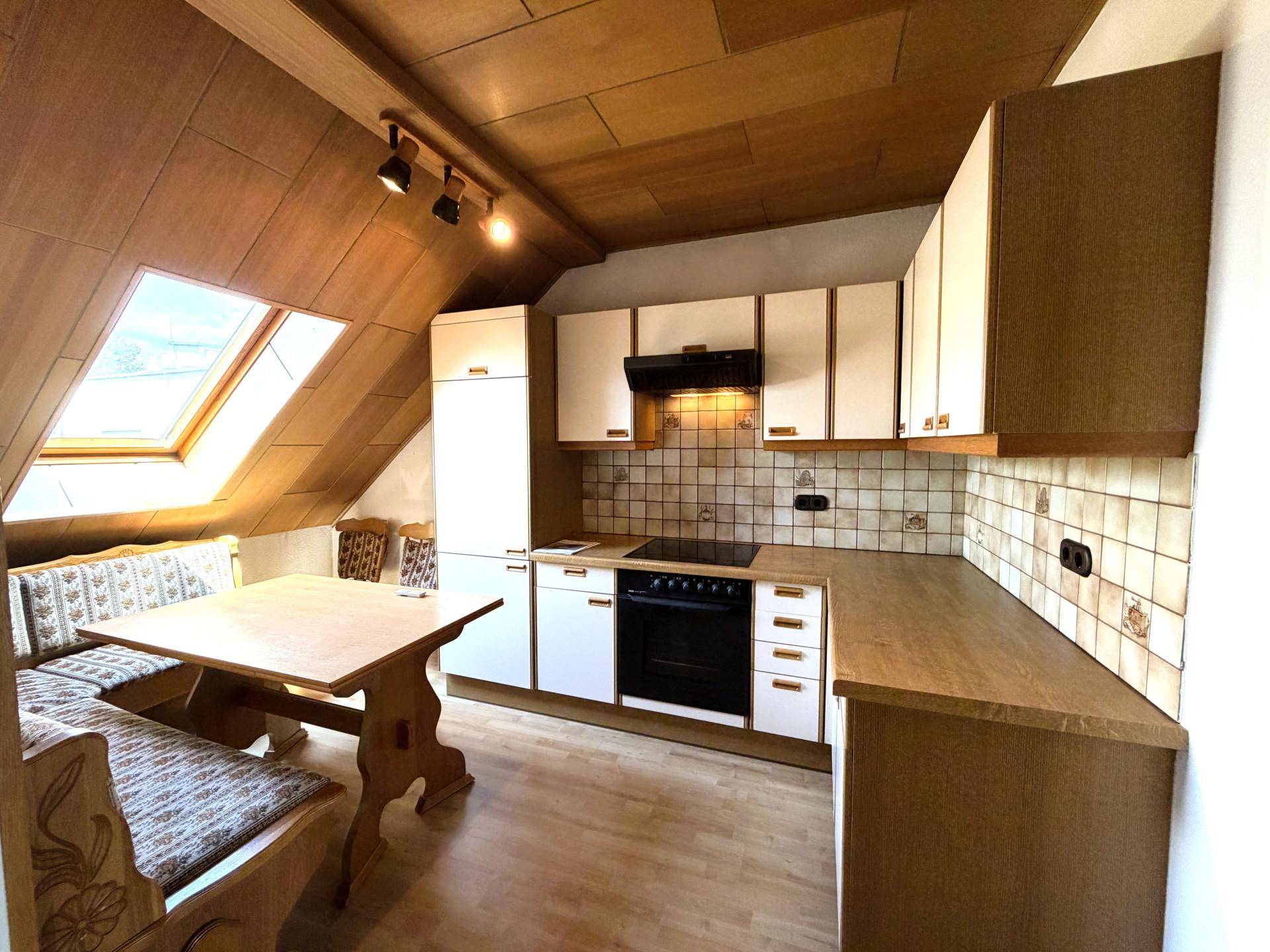 Dachgeschossküche mit Holzdachschrägen, Dachfenster und gemütlicher Essecke.