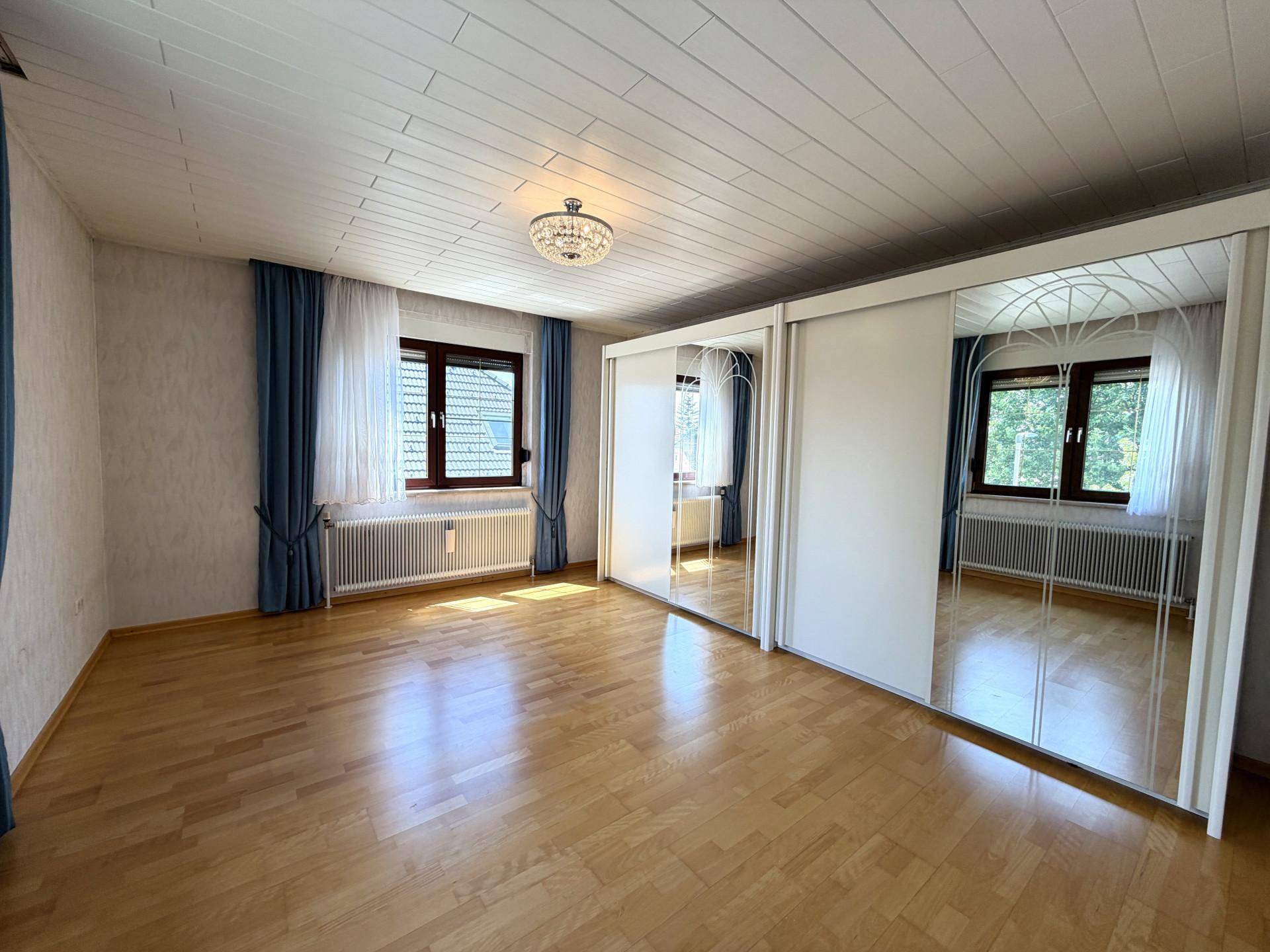 Helles Schlafzimmer mit Holzboden, Spiegelschränken und blauen Vorhängen.
