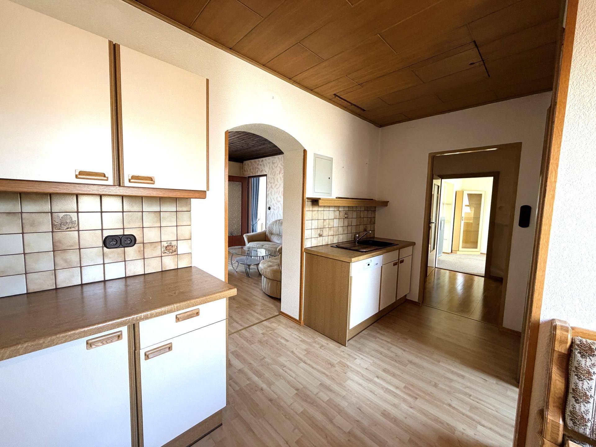 Kleine Küchenzeile mit weißen Schränken, Fliesenrückwand und Holzboden.