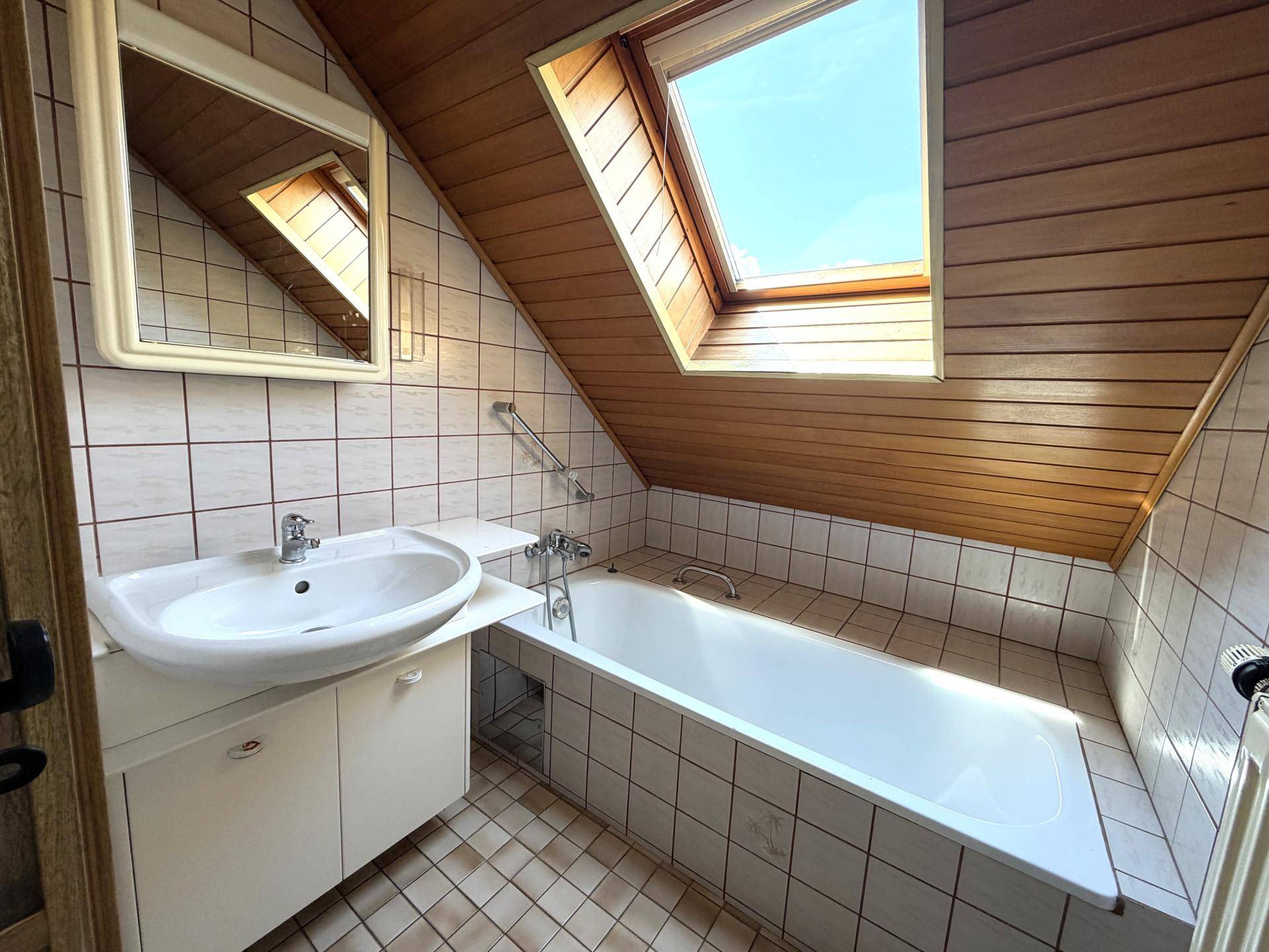 Dachgeschoss-Badezimmer mit Badewanne, Dachfenster und Holzdecke.