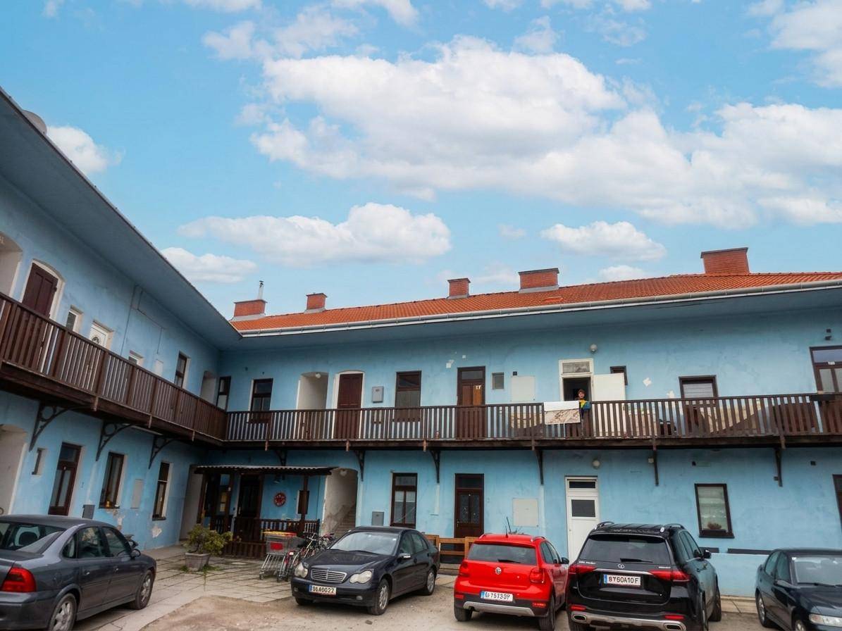 Innenhof eines blauen Gebäudes mit geparkten Autos und Holzbalkonen.
