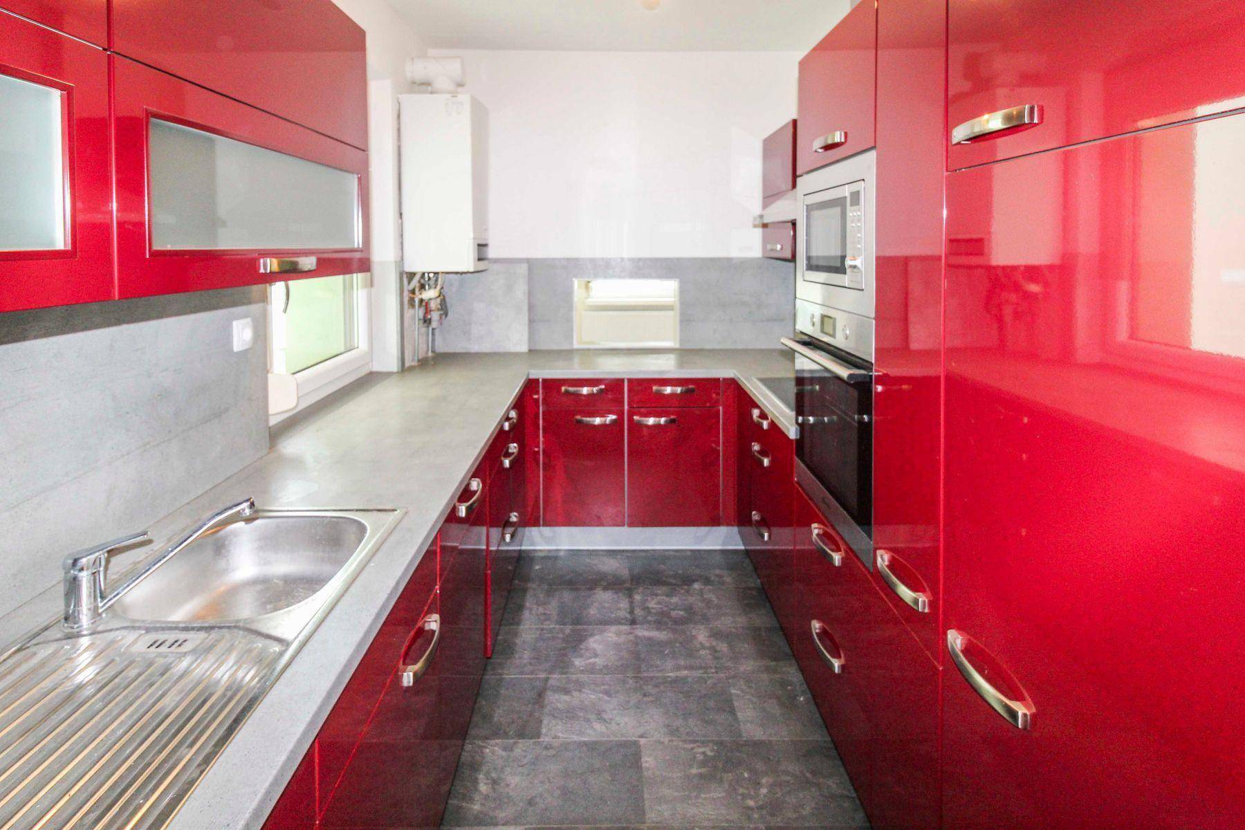 Moderne Küche mit glänzenden roten Schränken, grauen Arbeitsplatten und integrierten Geräten.