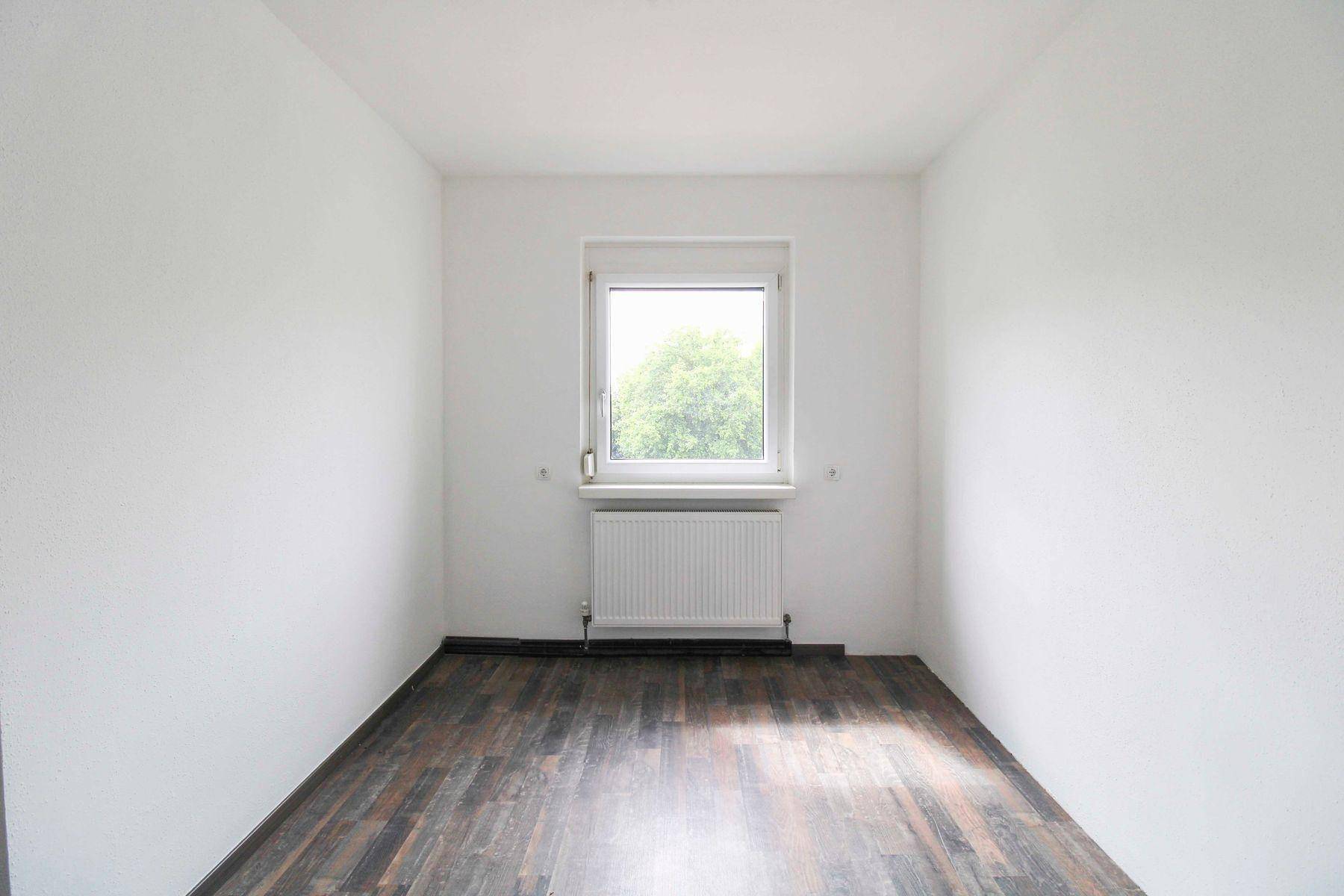 Kleines, helles Zimmer mit Holzoptikboden und einem Fenster, ideal als Schlaf- oder Arbeitszimmer.
