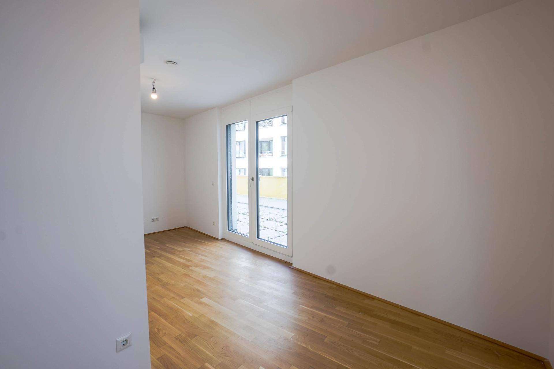 Geräumiger, heller Raum mit Parkettboden und Zugang zu einem Außenbereich durch große Glastüren.