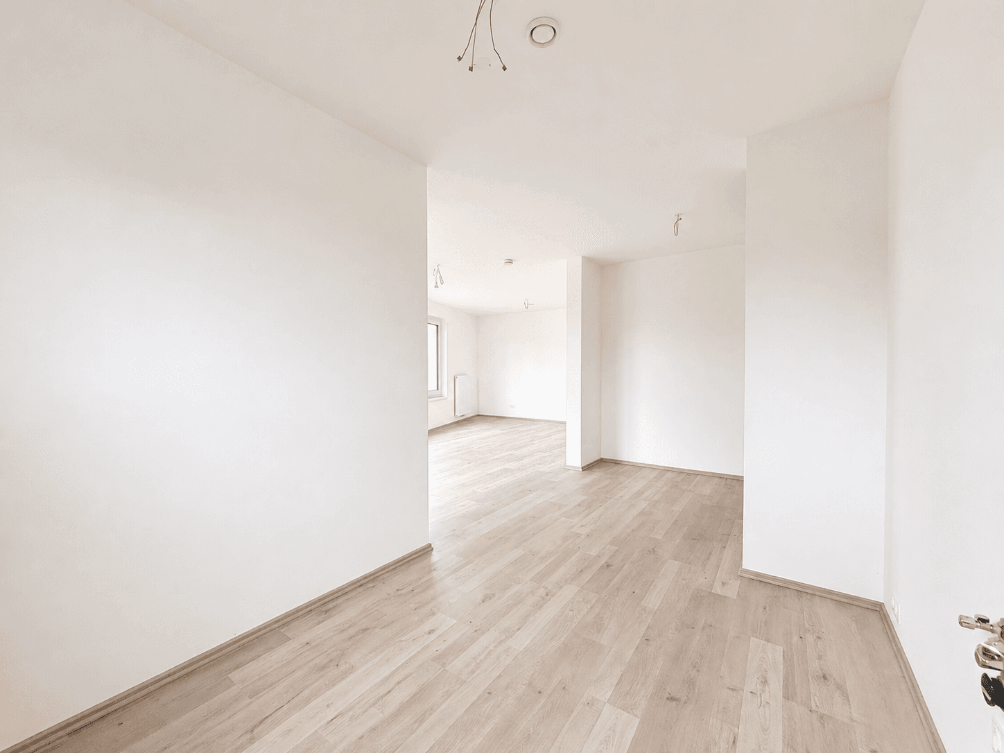 Heller Flur mit Laminatboden, der zu weiteren leeren Räumen in der Neubauwohnung führt.