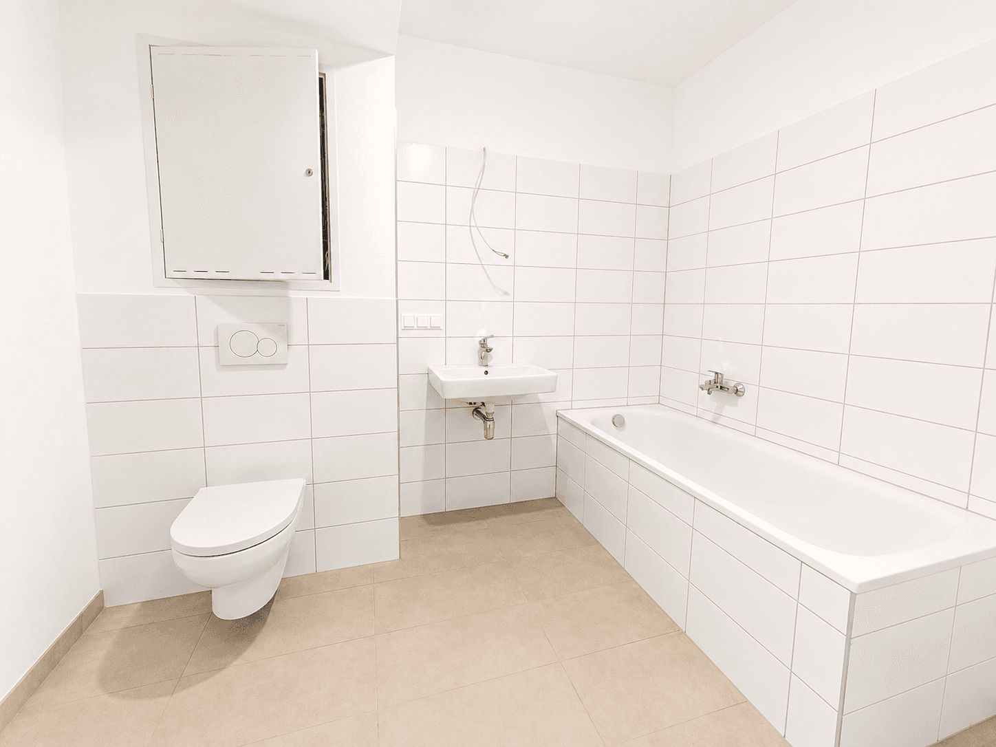 Modernes Badezimmer mit weißen Wand- und Bodenfliesen, Badewanne, Waschbecken und wandhängendem WC.