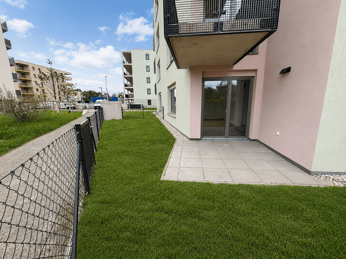 Gepflasterte Terrasse mit angrenzender Rasenfläche vor einem modernen Neubaugebäude.