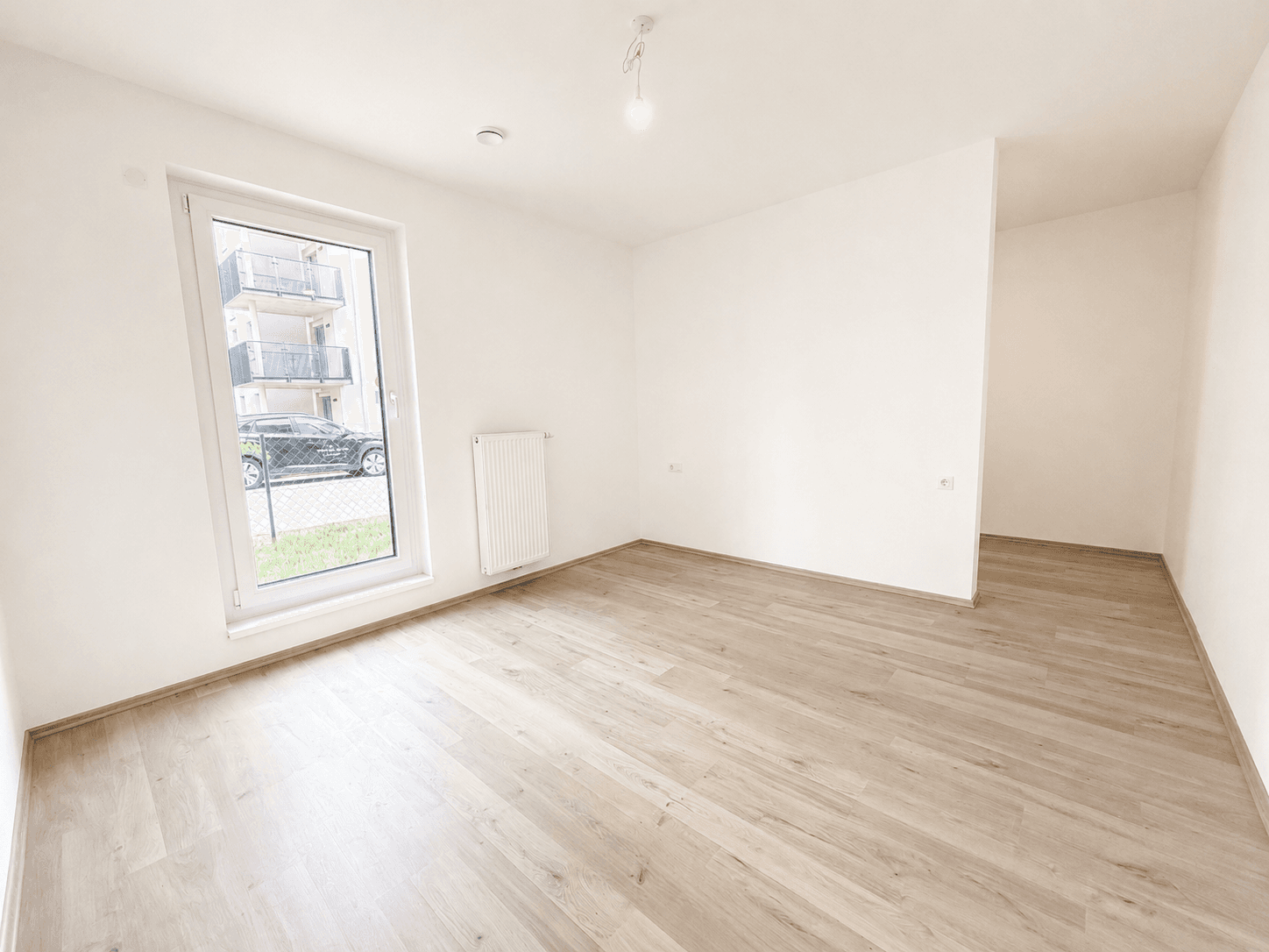 Leeres Schlafzimmer mit Laminatboden und einem Fenster mit Blick auf die Umgebung.