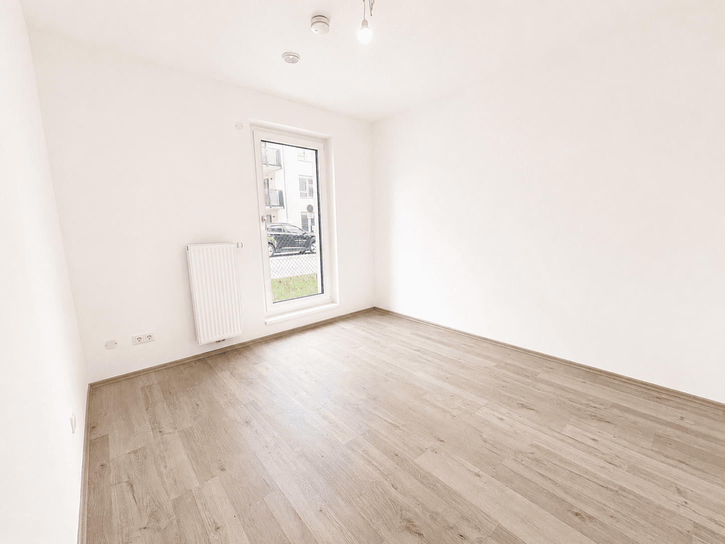 Unmöbliertes Zimmer mit Laminatboden und einem Fenster, das Tageslicht spendet.