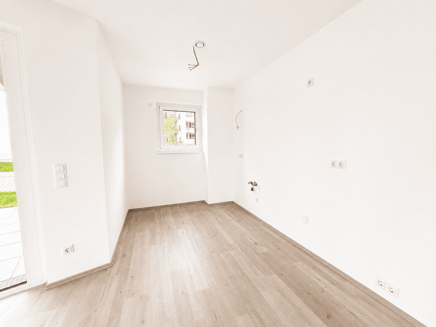 Leere Küche mit Laminatboden und Anschlüssen für eine Einbauküche.