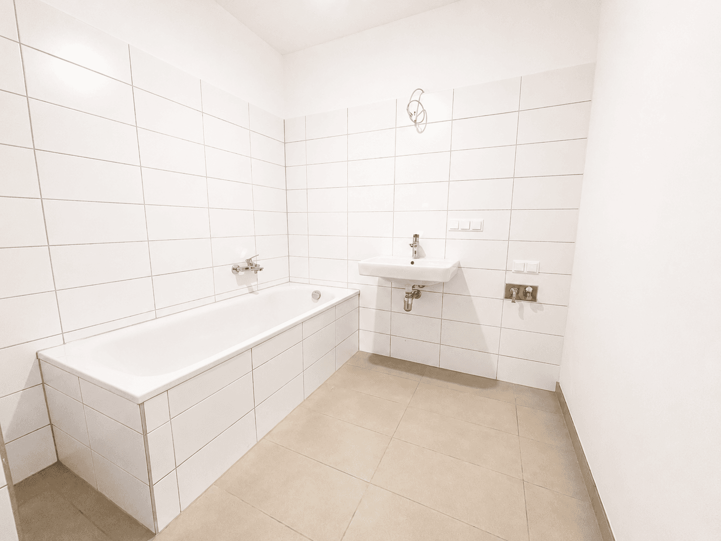 Modernes Badezimmer mit weißen Fliesen, Badewanne und Waschbecken.