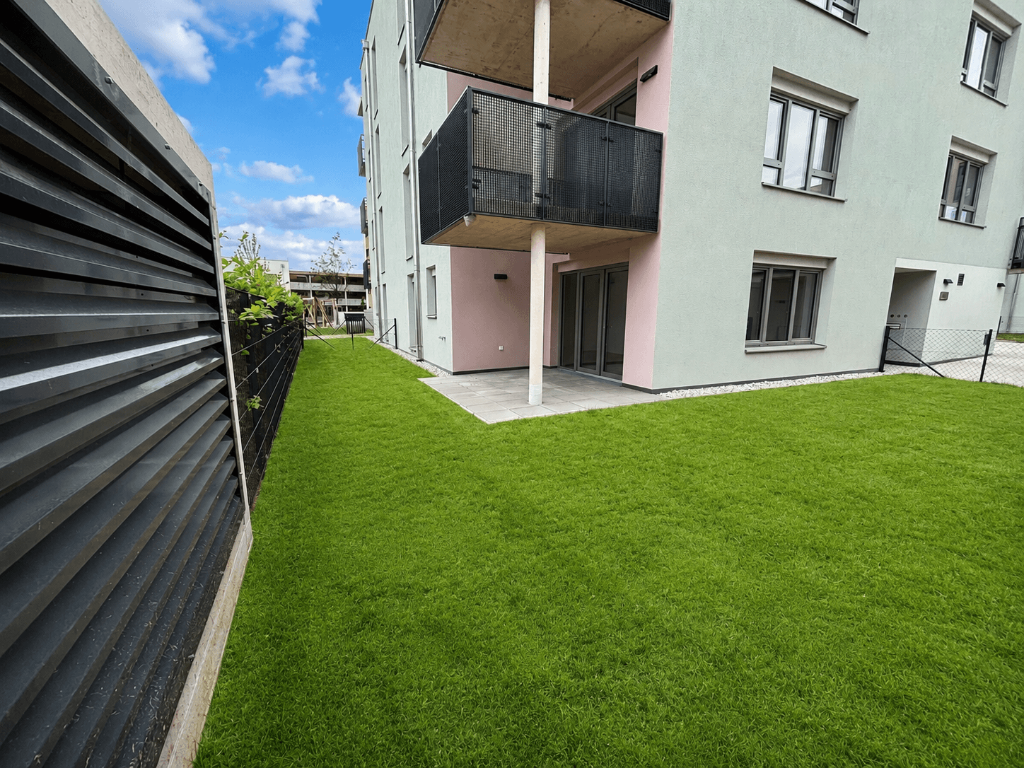 Gepflegter Rasenbereich mit kleiner Terrasse vor einem modernen Mehrfamilienhaus.