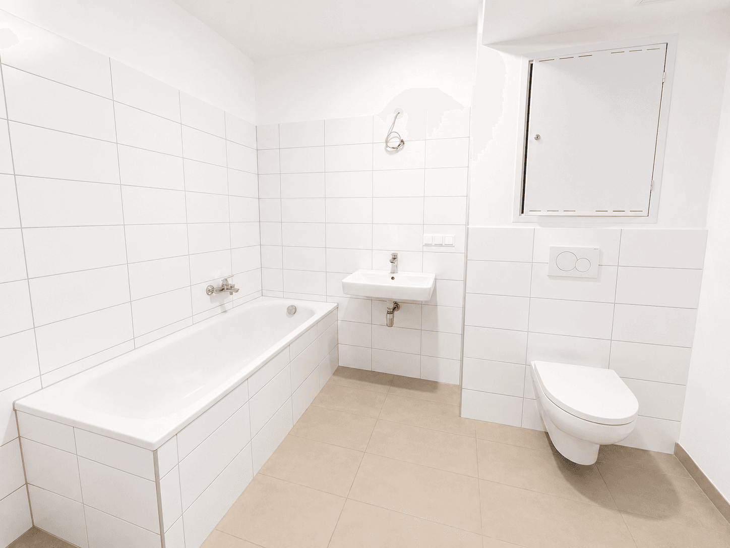 Modernes Badezimmer mit weißen Fliesen, Badewanne, Waschbecken und wandhängendem WC.