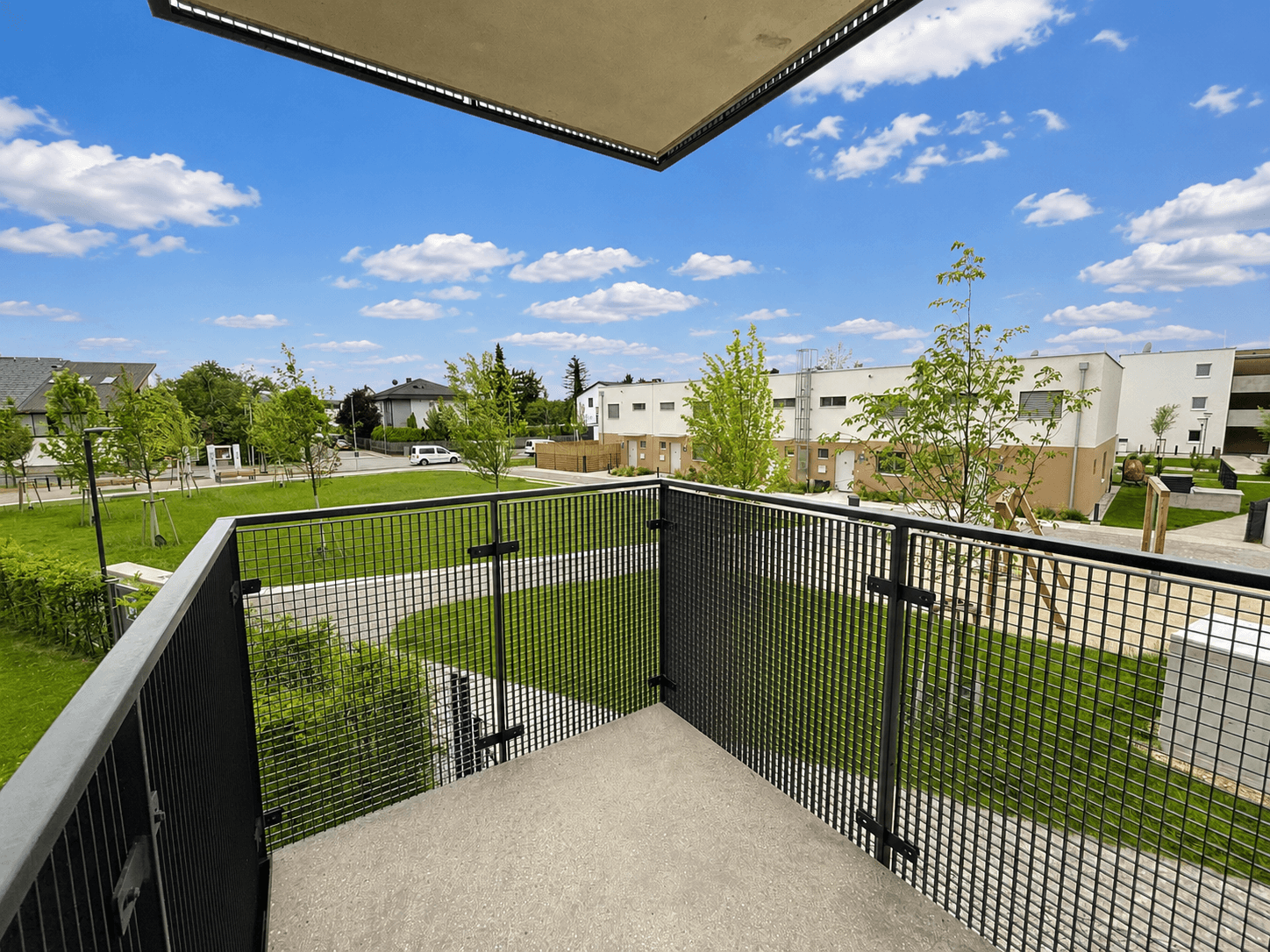 Balkon mit Metallgeländer und Blick auf eine moderne Wohnsiedlung mit Grünflächen.
