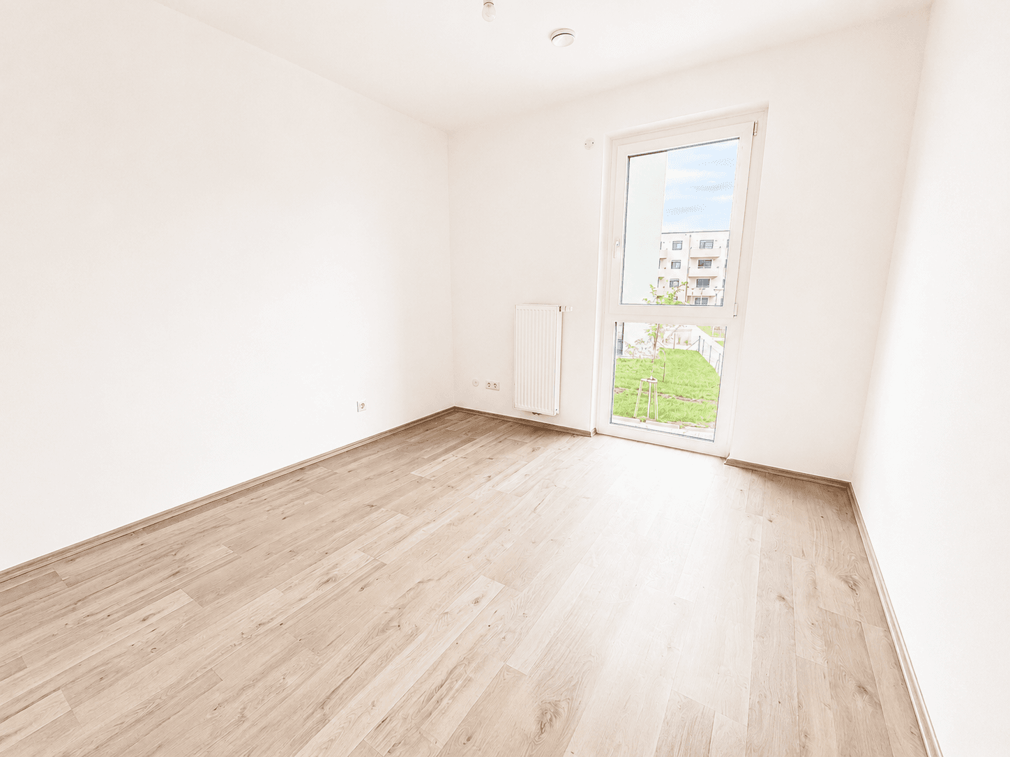 Leeres Schlafzimmer mit hellem Laminatboden und direktem Zugang zu einem kleinen Gartenbereich.