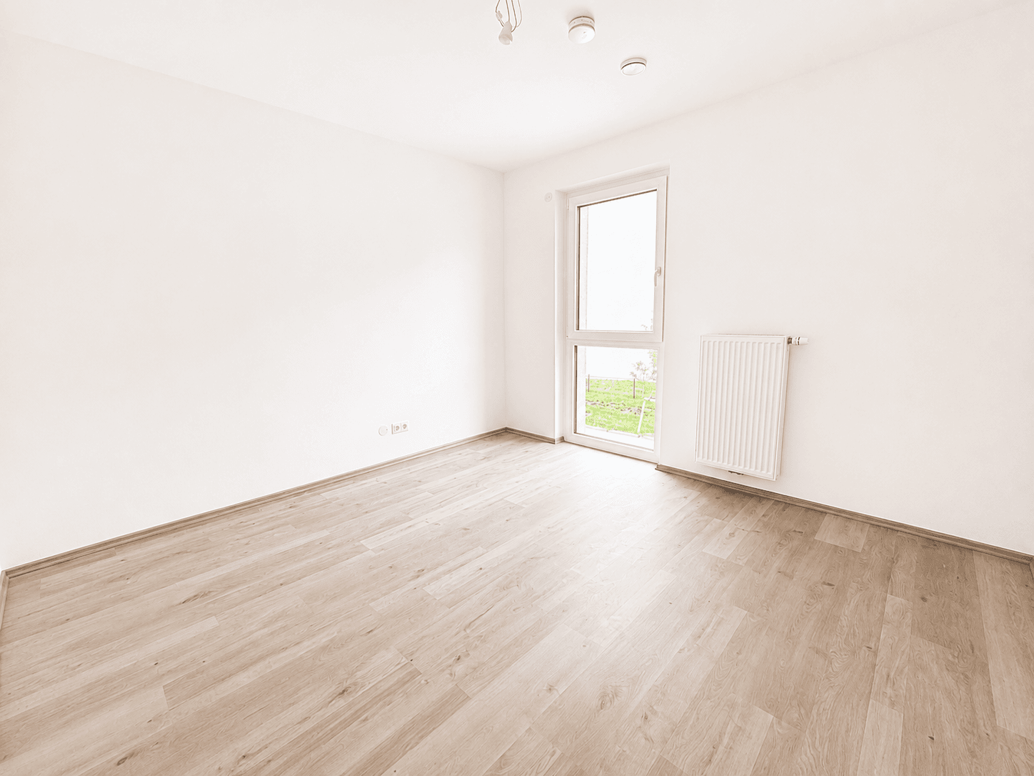 Leeres Schlafzimmer mit hellem Laminatboden und einem Fenster mit Blick ins Grüne.