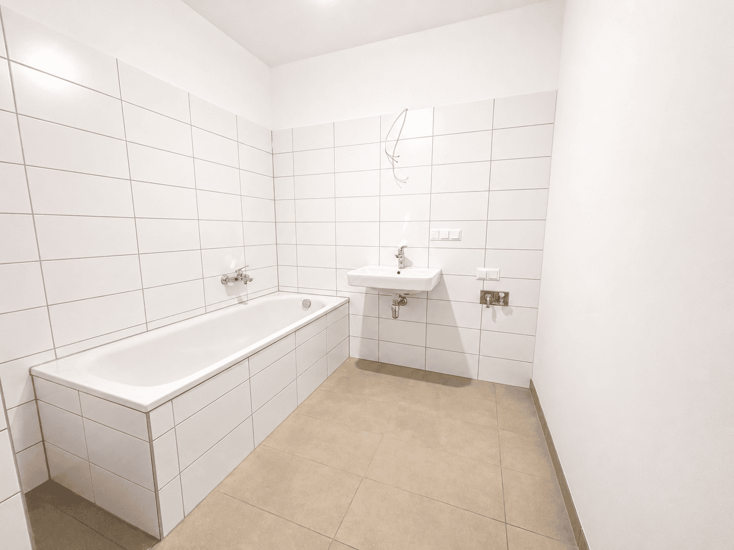 Modernes Badezimmer mit weißen Fliesen, Badewanne und Waschbecken, bereit zur Fertigstellung.