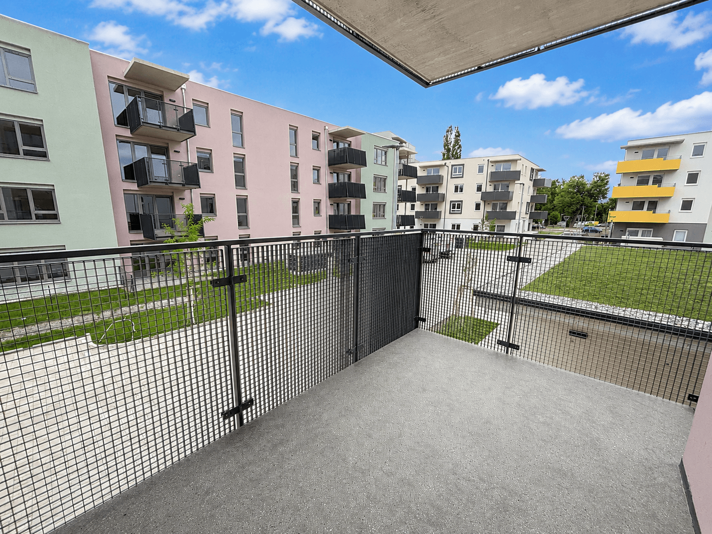 Balkon mit Blick auf moderne Wohngebäude und grüne Innenhöfe in einer Neubauanlage.