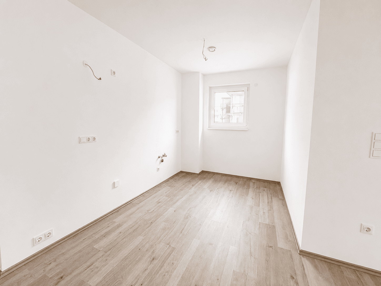 Leerer Raum, vorbereitet für eine Küche, mit Laminatboden und Fenster.
