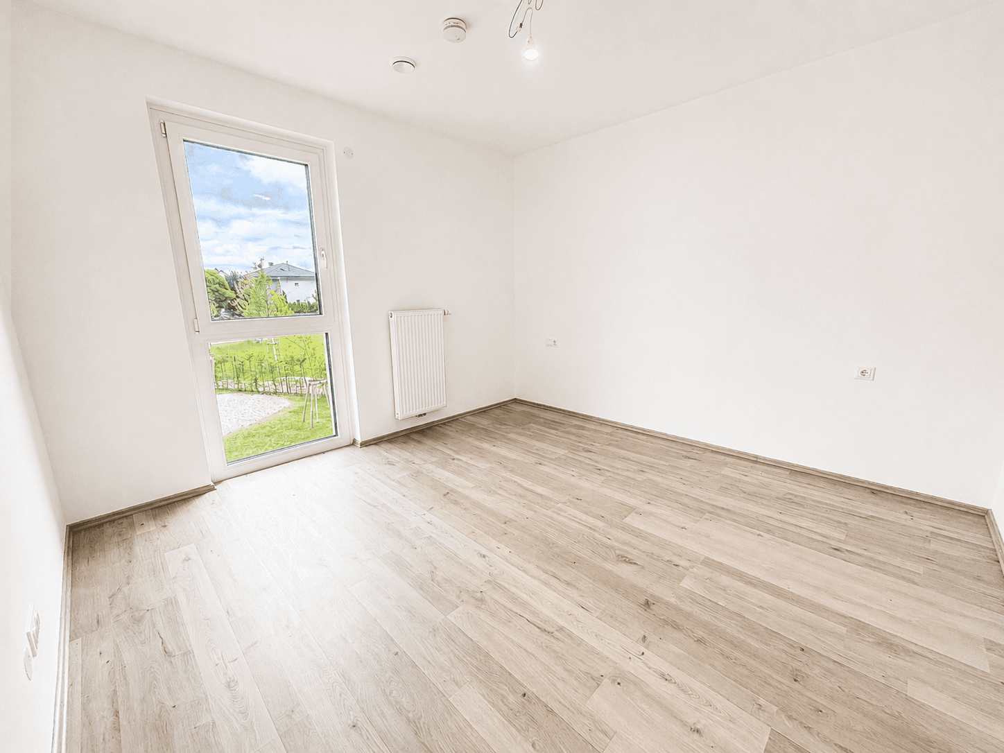 Helles Zimmer mit Laminatboden und Zugang zu einem kleinen Gartenbereich.