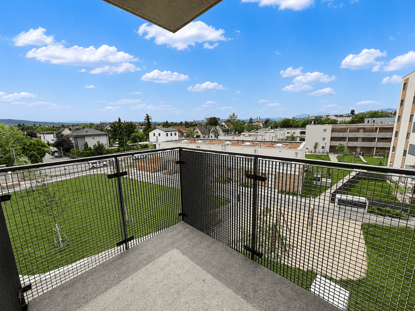 Balkon mit Blick auf eine grüne Wohnanlage und die umliegende Nachbarschaft.