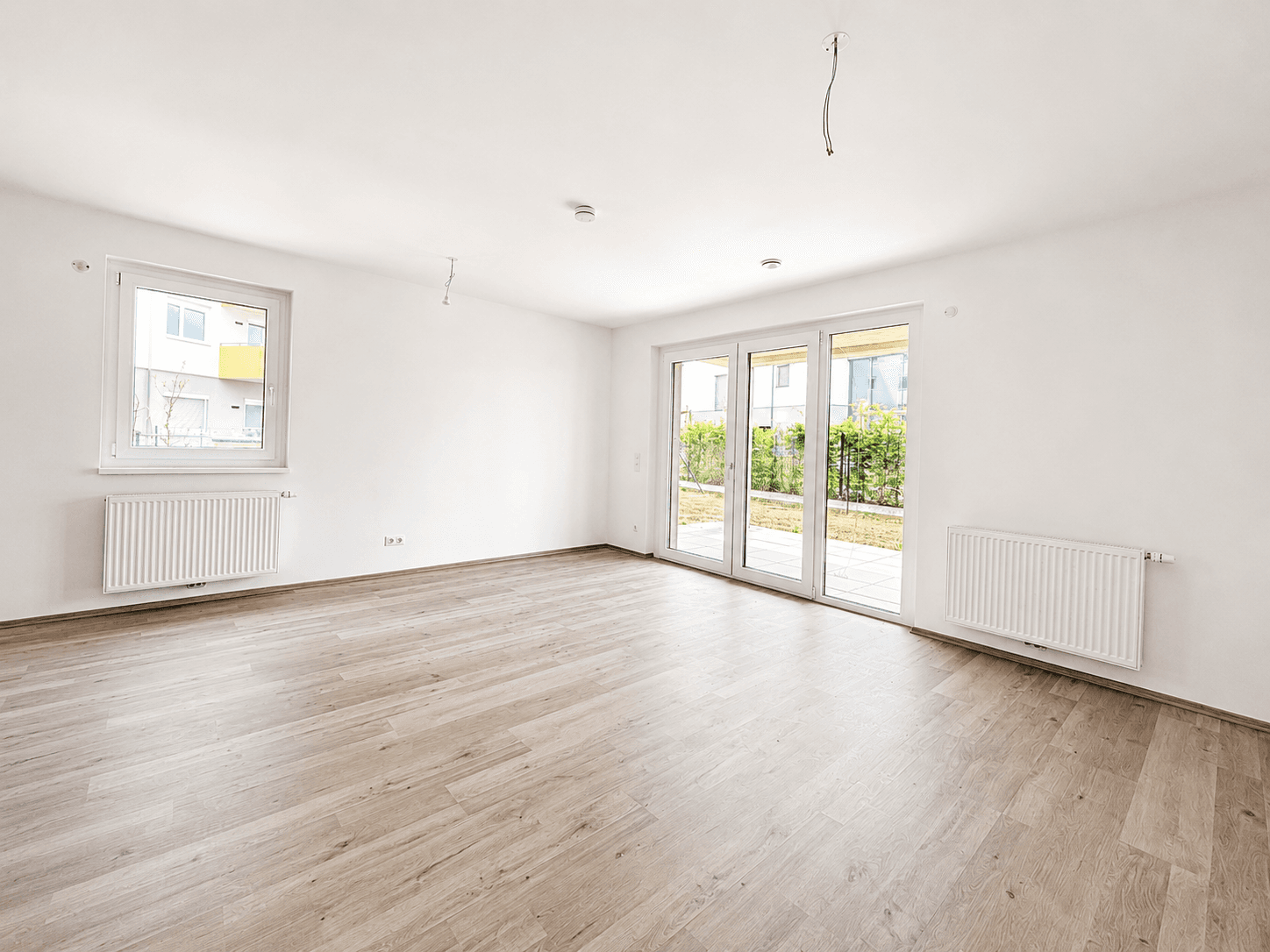Heller Wohnraum mit großem Fenster, Schiebetüren zum Garten und Laminatboden.