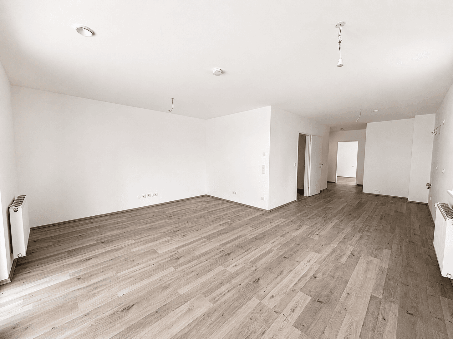 Geräumiger, heller Wohnbereich mit Laminatboden und weißen Wänden in einem Neubau.