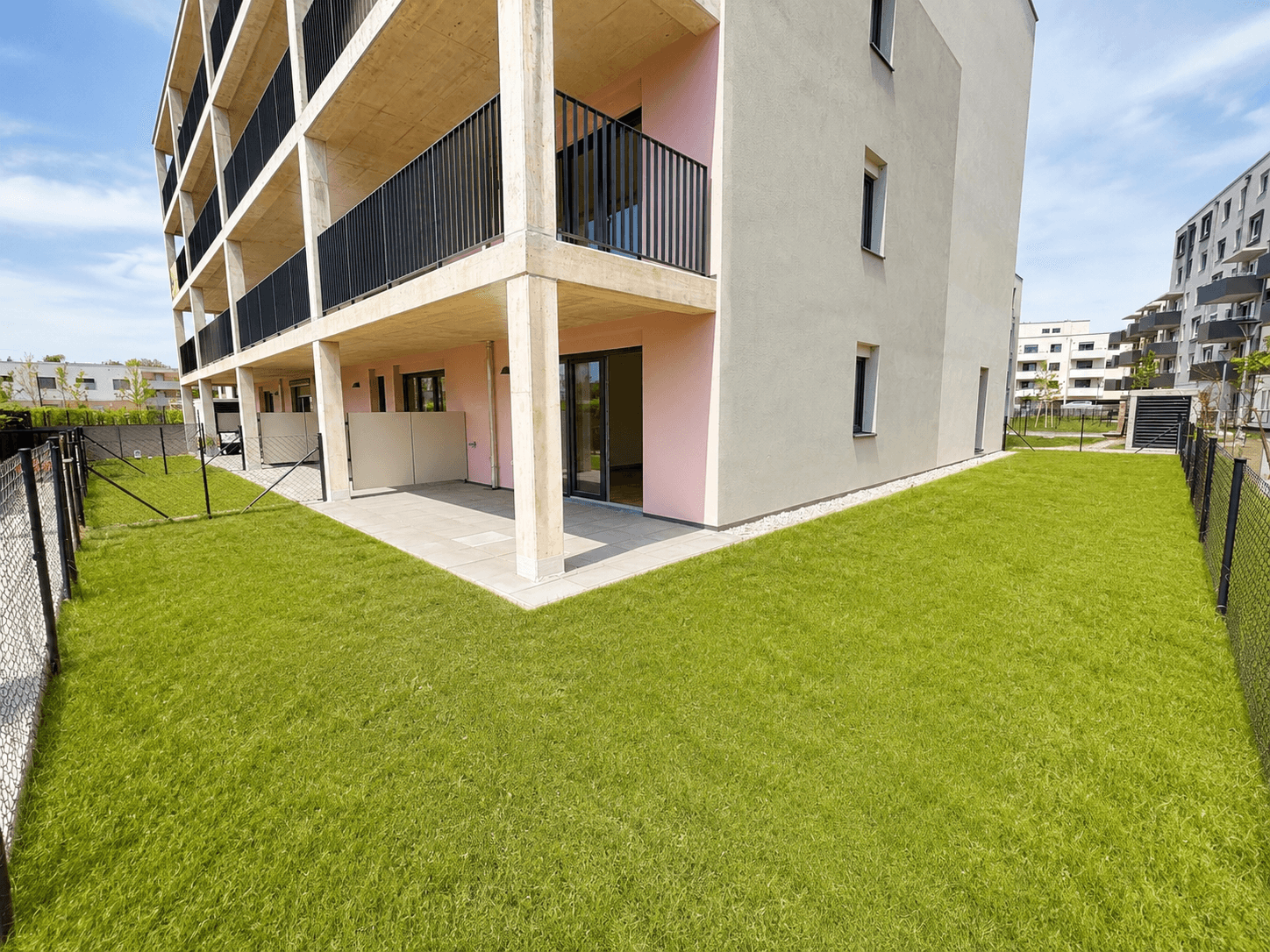 Moderne Gebäudefassade mit Balkonen, einer Terrasse und einem gepflegten Rasenbereich.