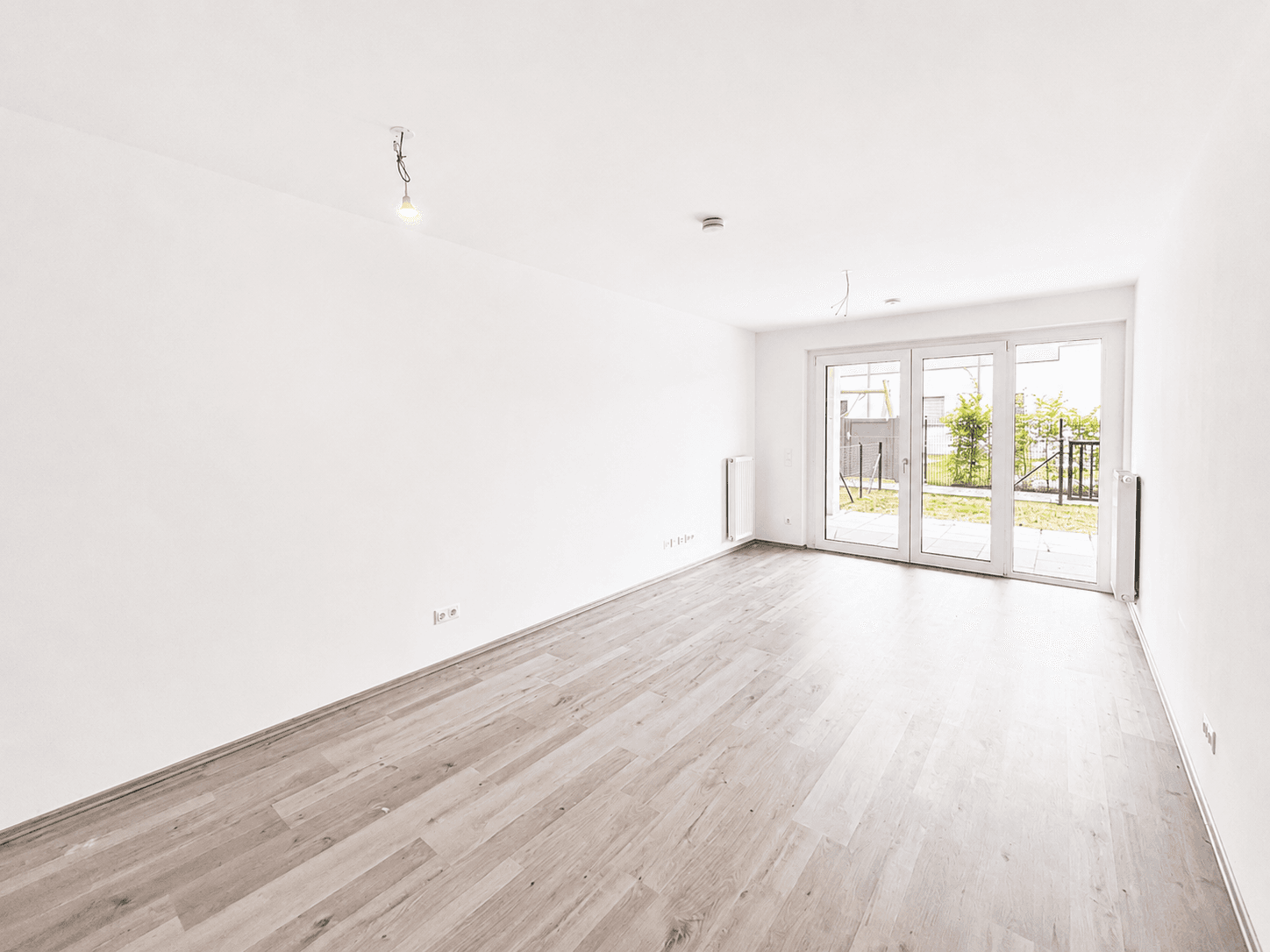 Geräumiges, helles Wohnzimmer mit Laminatboden und großen Fenstertüren, die viel Tageslicht hereinlassen.