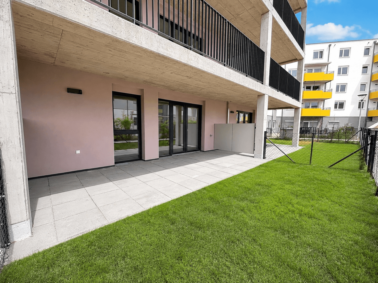 Erdgeschoss-Terrasse mit gepflastertem Bereich und angrenzender Rasenfläche vor einem modernen Gebäude.