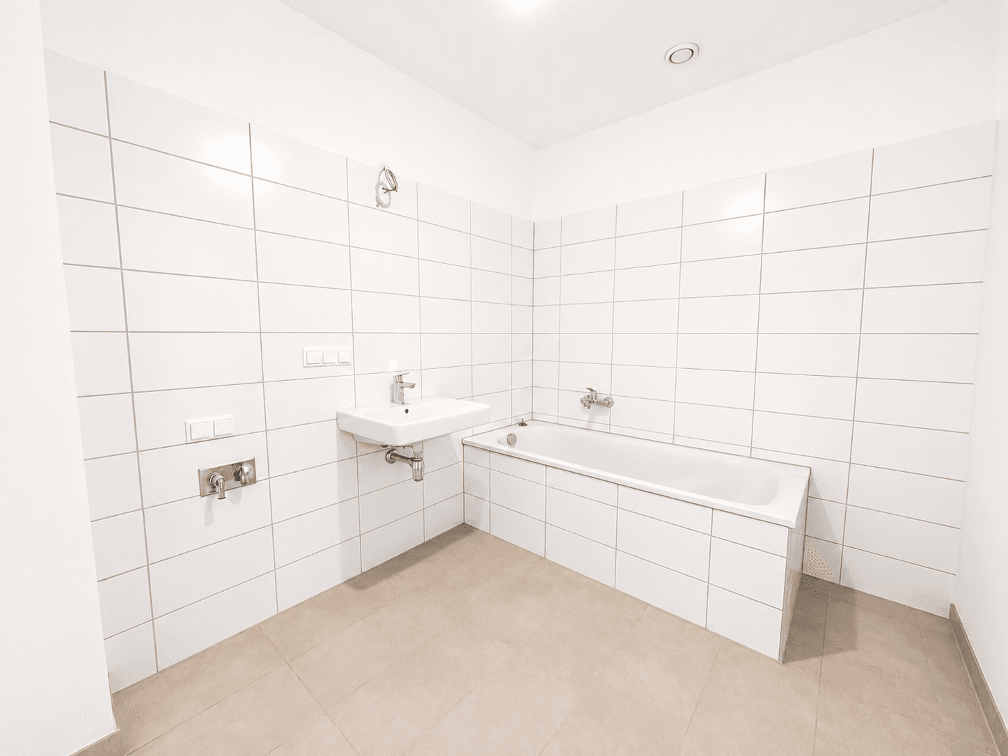 Modern gefliestes Badezimmer mit Badewanne und Waschbecken in neuwertigem Zustand.
