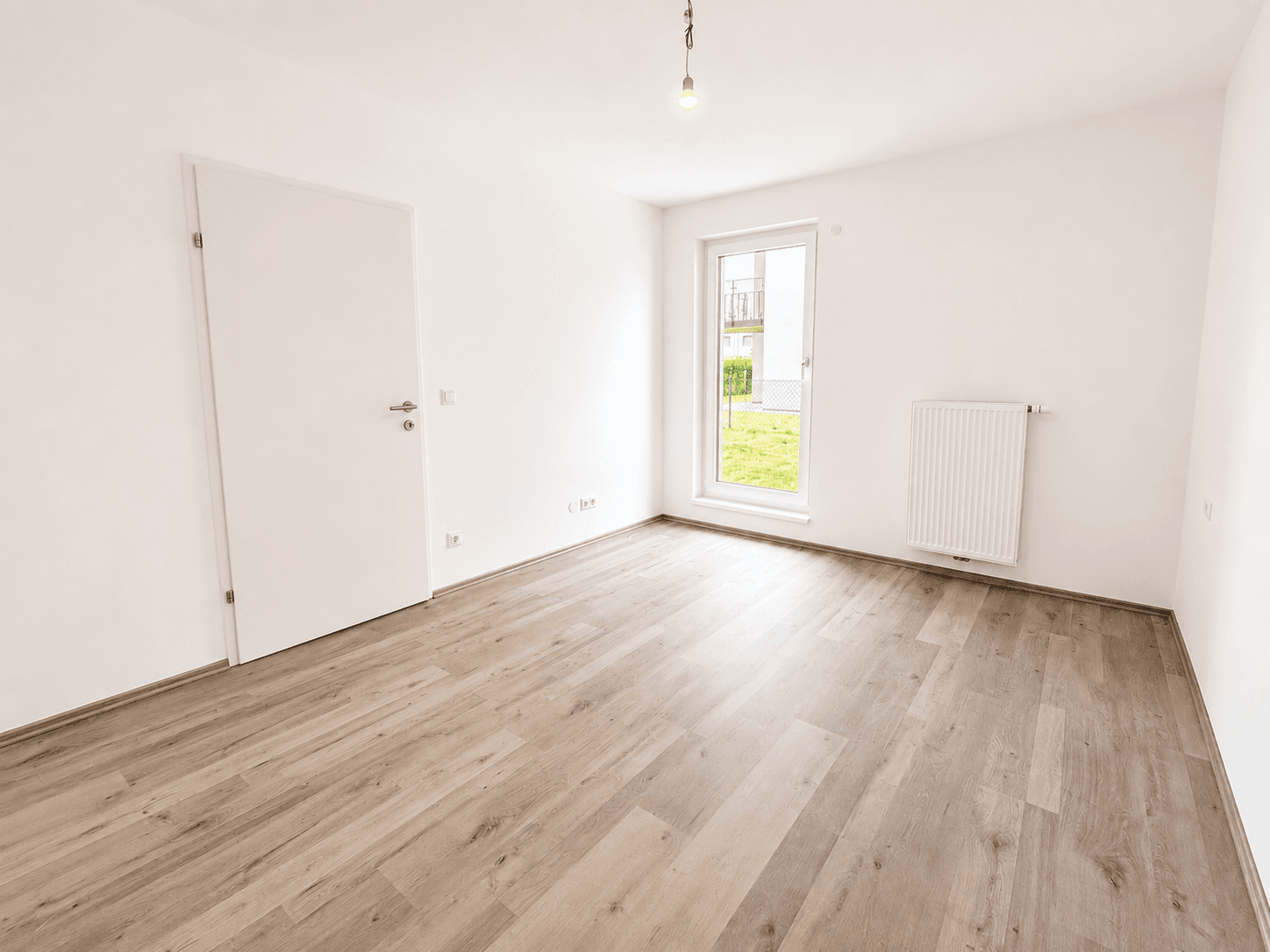 Kleinerer, heller Raum mit Laminatboden und einem Fenster, geeignet als Schlaf- oder Arbeitszimmer.