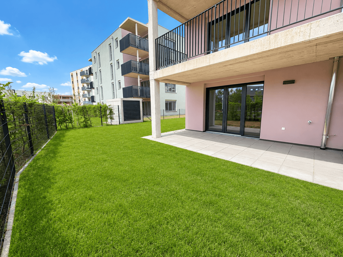 Gepflegter Gartenbereich mit Rasenfläche und einer Terrasse vor einem modernen Neubau.
