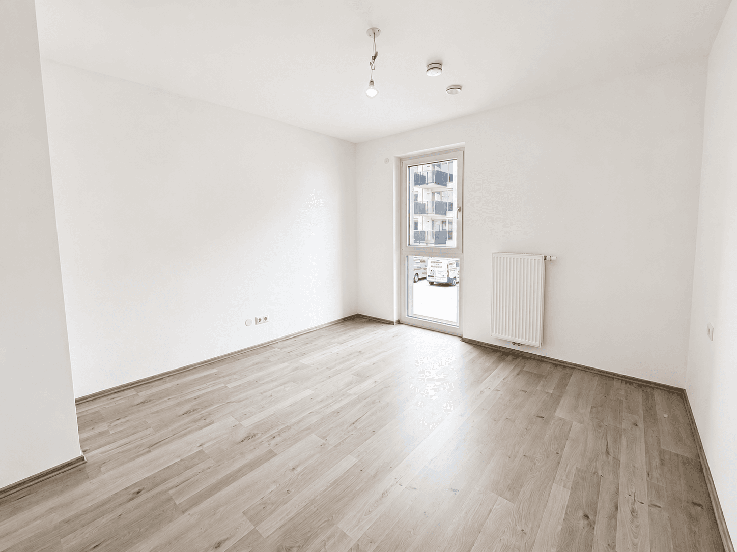 Helles Schlafzimmer mit Laminatboden, weiß gestrichenen Wänden und großem Fenster mit Blick nach draußen.