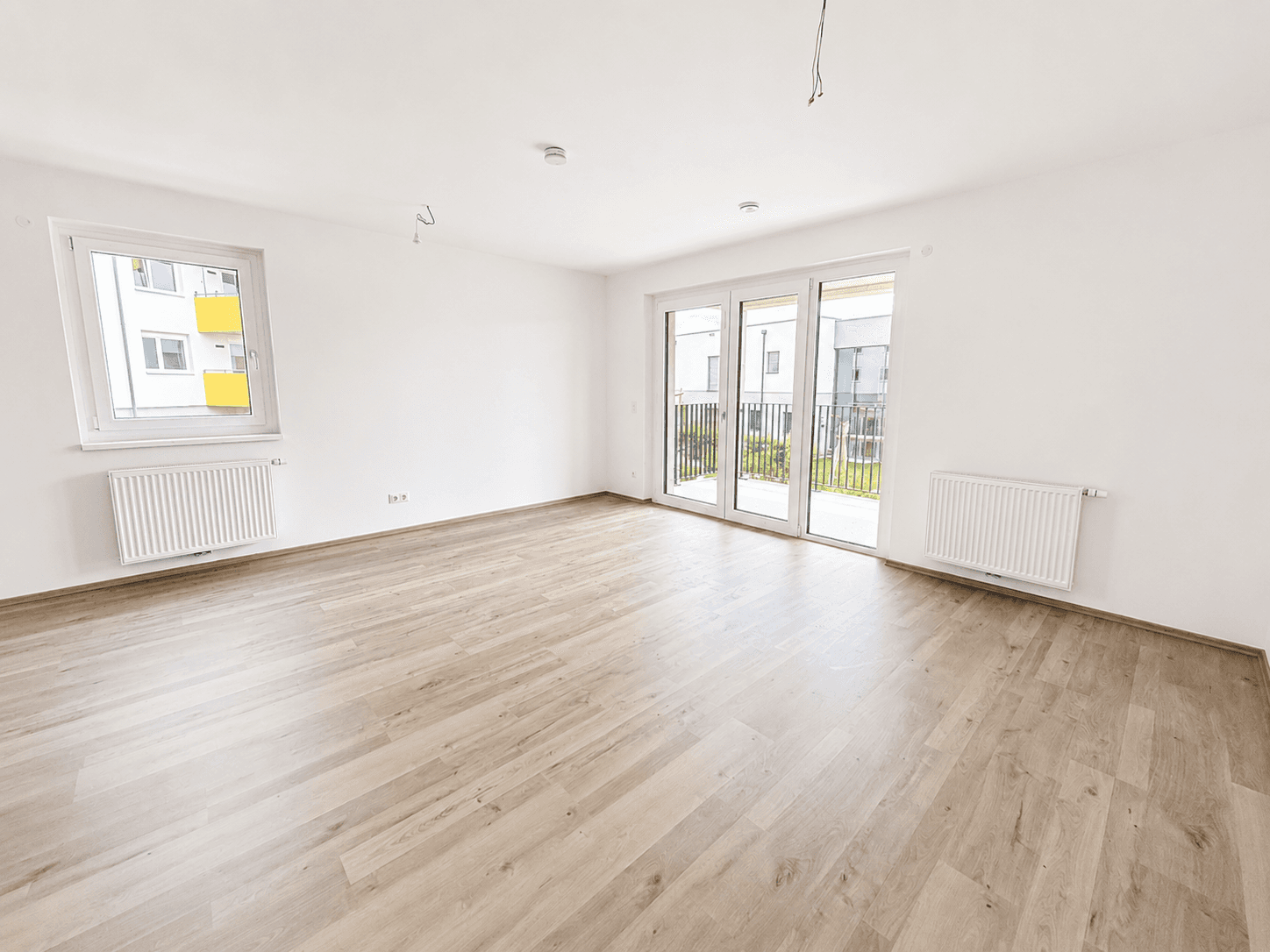 Heller Wohnraum mit Laminatboden, großen Fenstern und Zugang zum Balkon in einem Neubau.